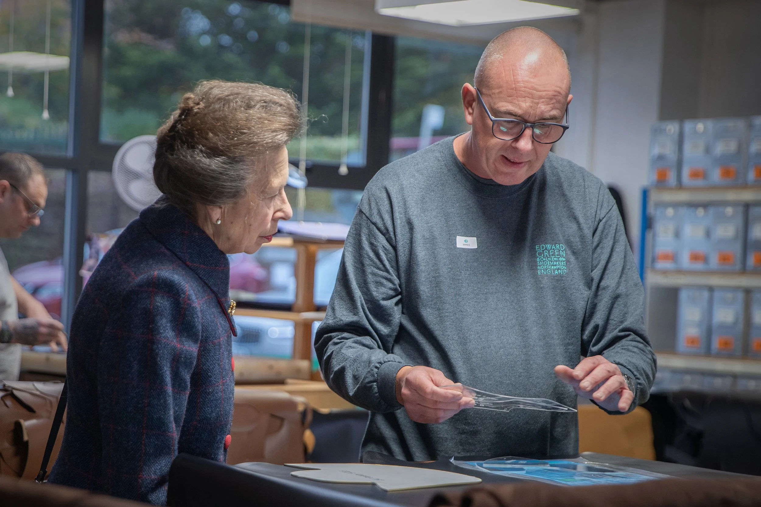 An elderly woman and a man with glasses examining a clear plastic item in a store with other people and shelves in the background.