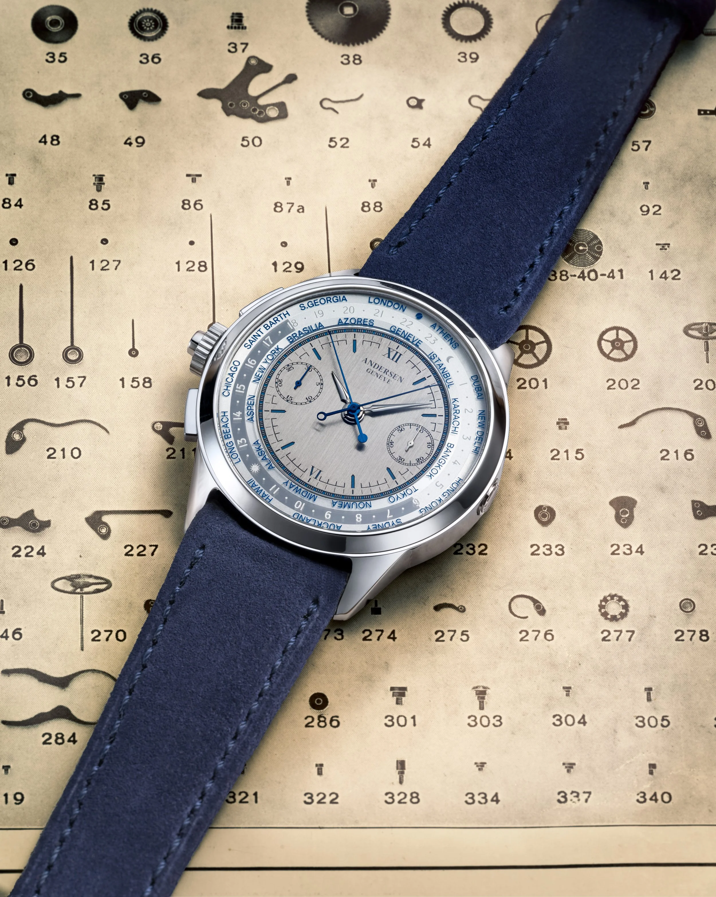 A silver wristwatch with a blue leather strap resting on an illustrated mechanical parts chart.
