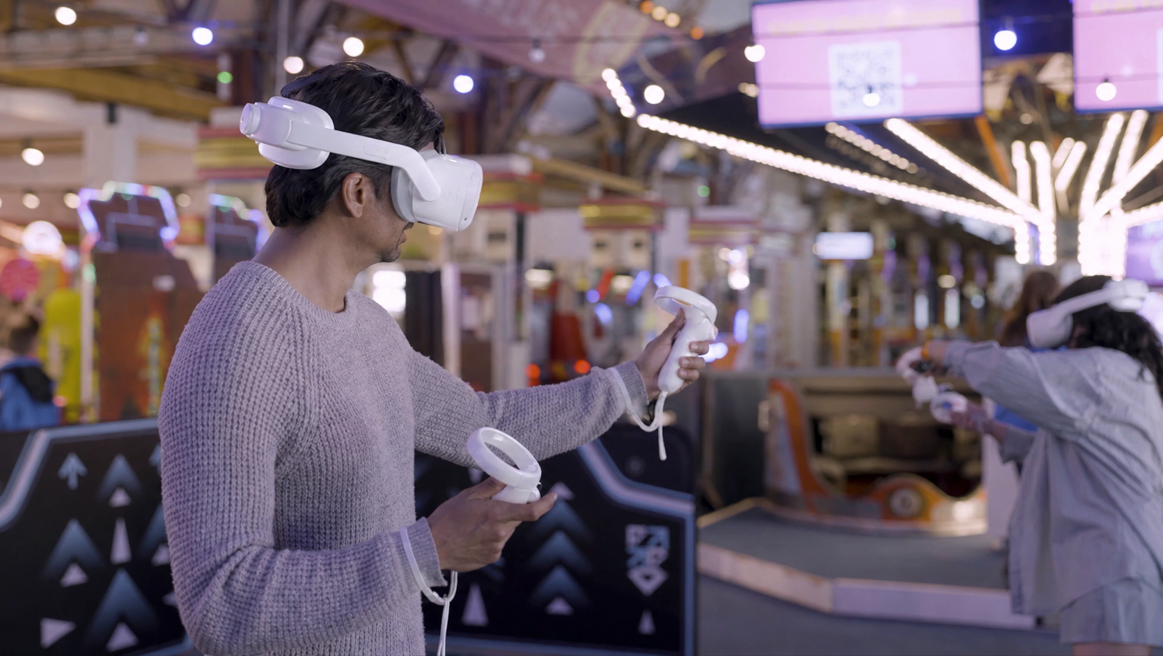 Hombre usando gafas de realidad virtual en una sala de juegos con luces y niños jugando en el fondo.