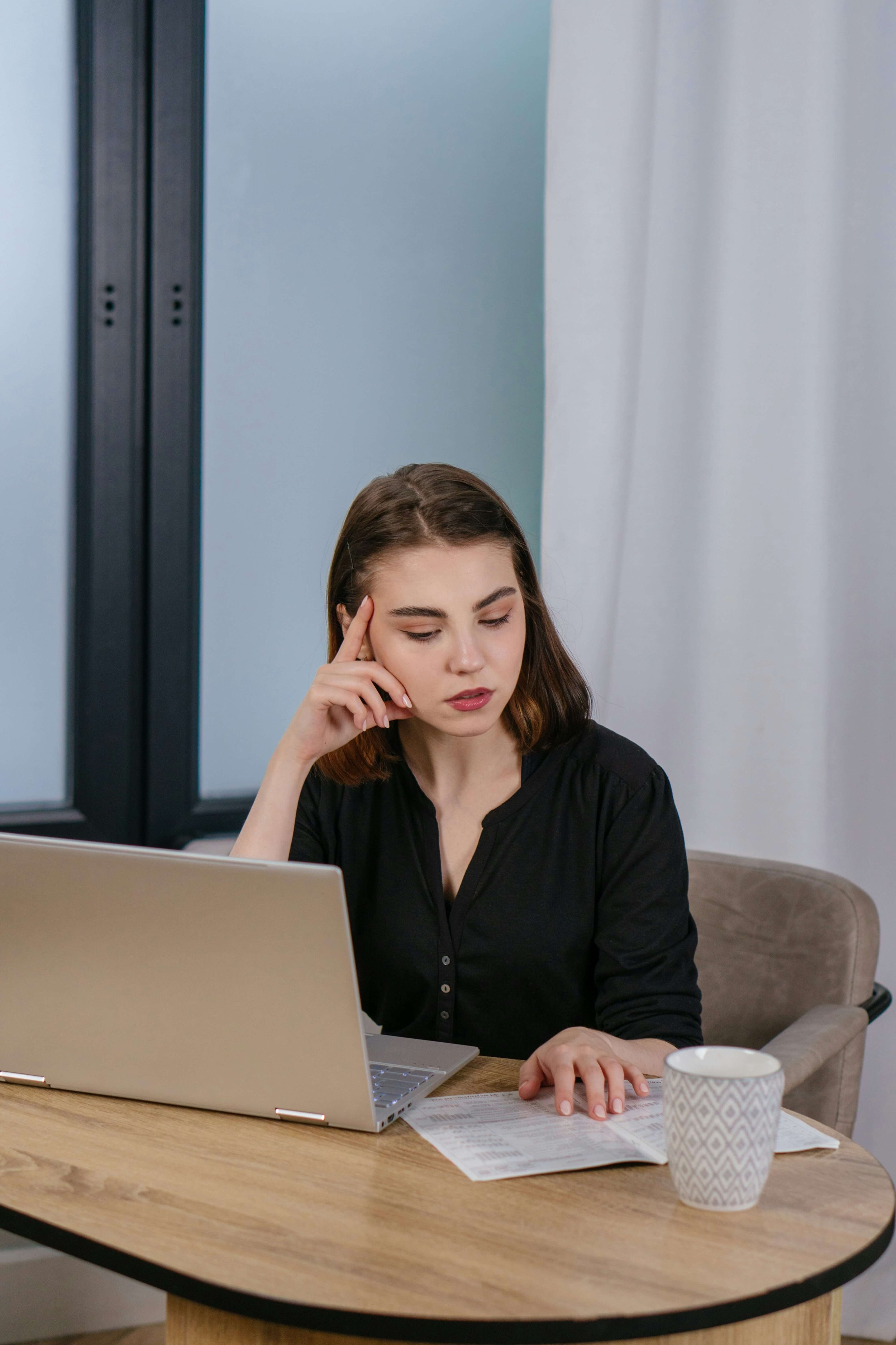 woman sitting at a table in a black top with a laptop, notebook and mug