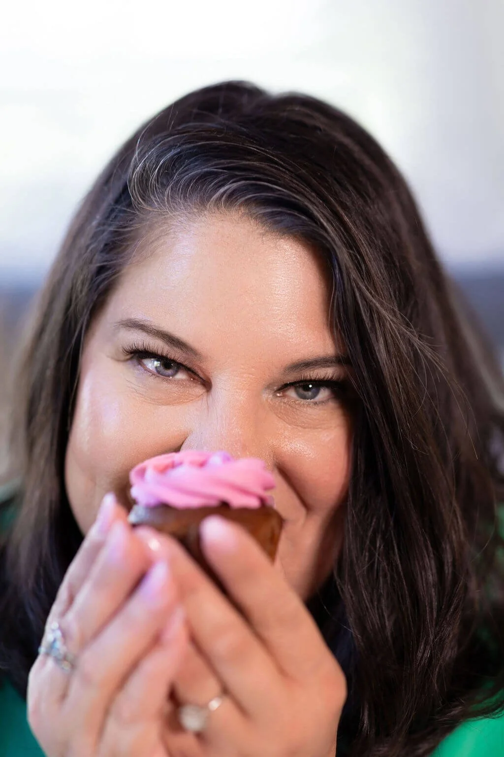 Woman with long brown hair and blue eyes holding a cupcake with pink icing.