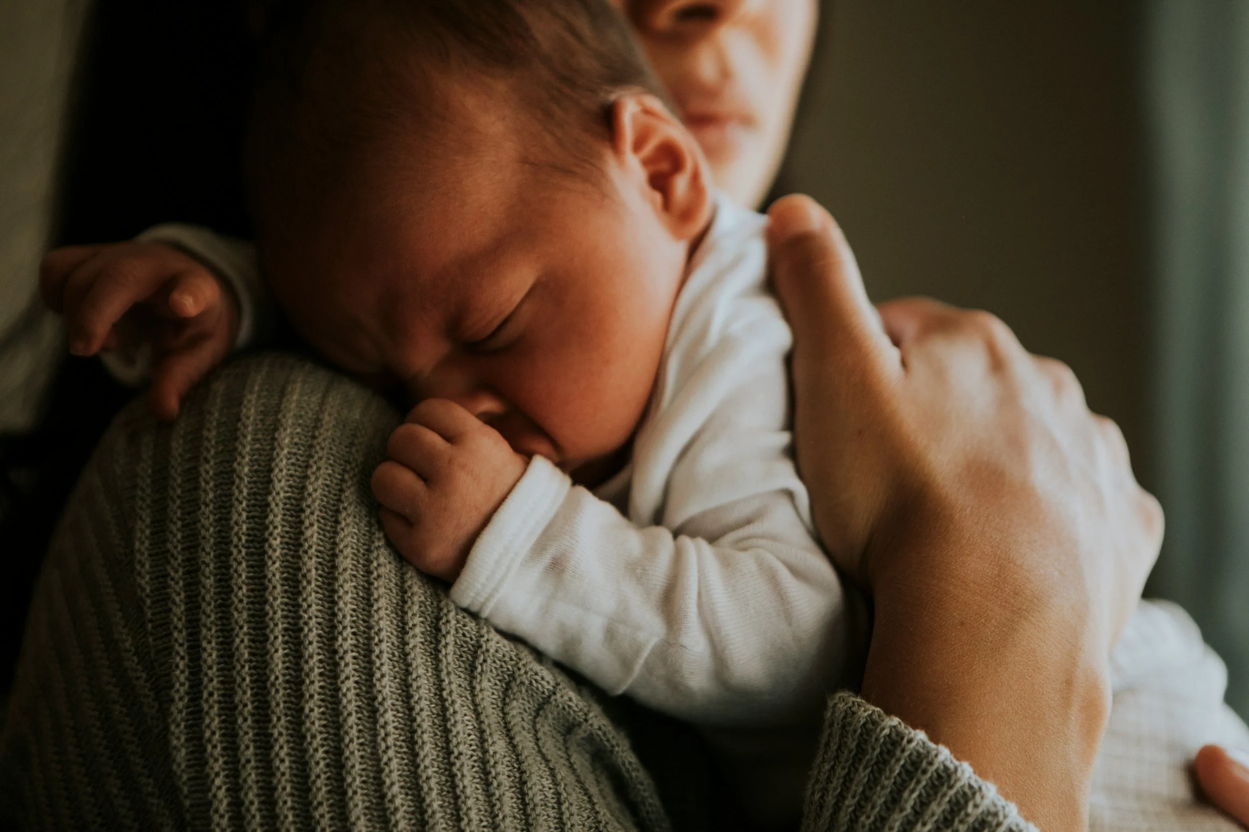 A person holding a sleeping baby close to their chest, with the baby's face nestled into the person's shoulder.