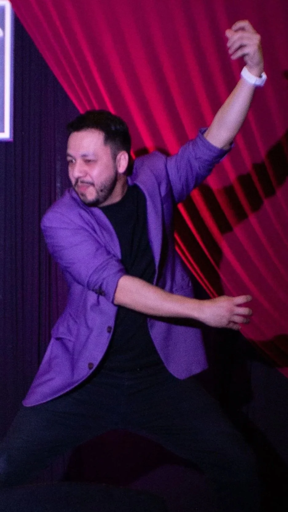Juancho Carbono con chaqueta morada bailando en un escenario durante una función del show de comedia "Fragmental" con cortinas rojas de fondo.