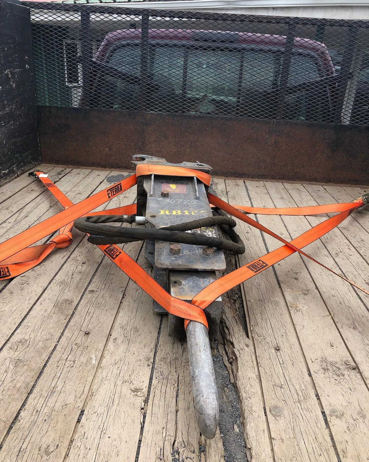 A skateboard with mounted attachments secured in a trailer with orange straps, on a wooden floor.
