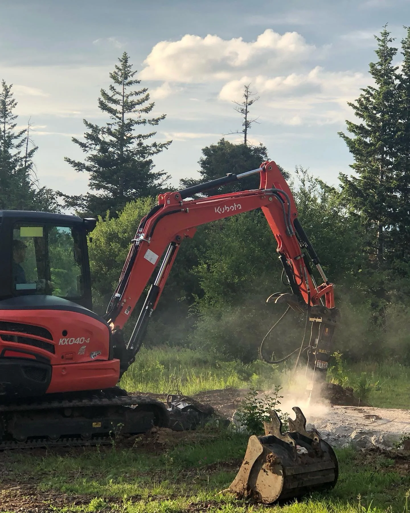 A Kubota excavator breaking up concrete with a hydraulic breaker.