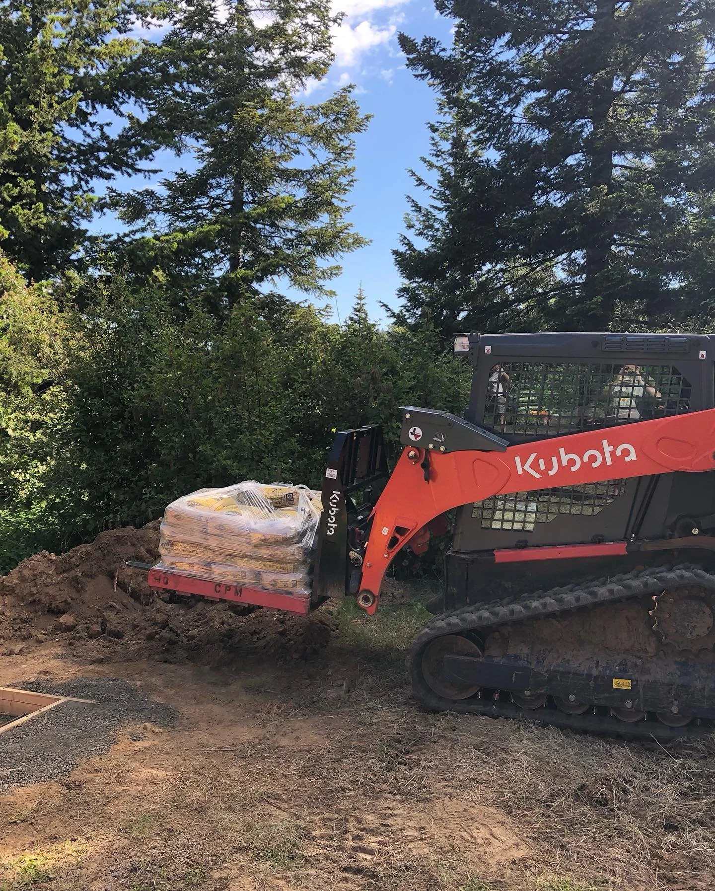 A Kubota skid steer is moving a pallet of concrete bags for a generator pad in a remote location.