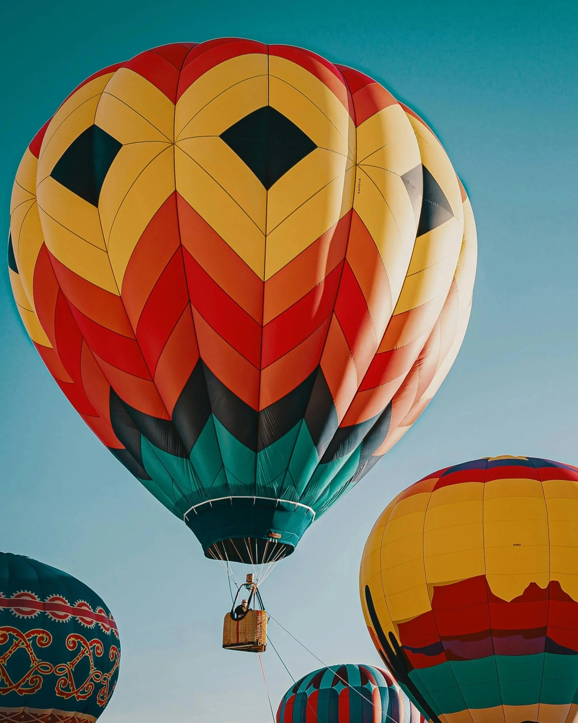 Multiple colorful hot air balloons floating in the sky, featuring unique and vibrant designs.