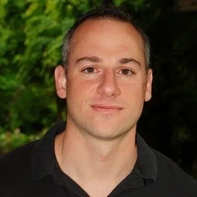 A portrait of a man with short dark hair in front of a green outdoor background.