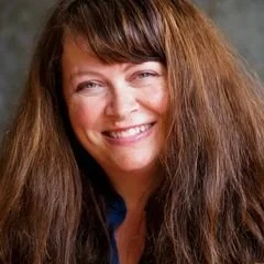 Close-up of a woman with long, curly brown hair smiling at the camera.