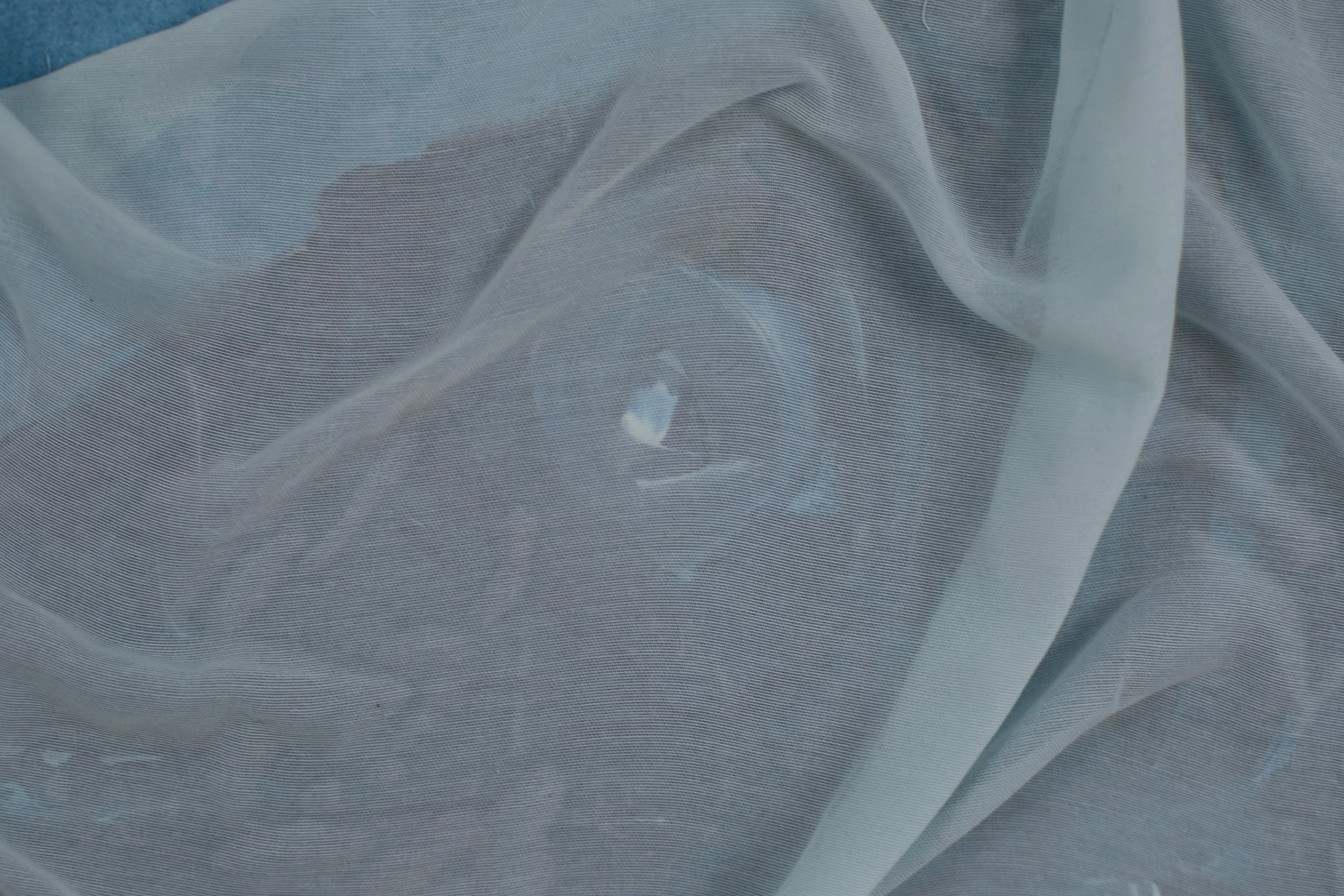 Nahaufnahme eines menschen, der hinter einem transparenten, leicht gewellten Stoff verborgen ist, mit einem Blick durch den Stoff hindurch.