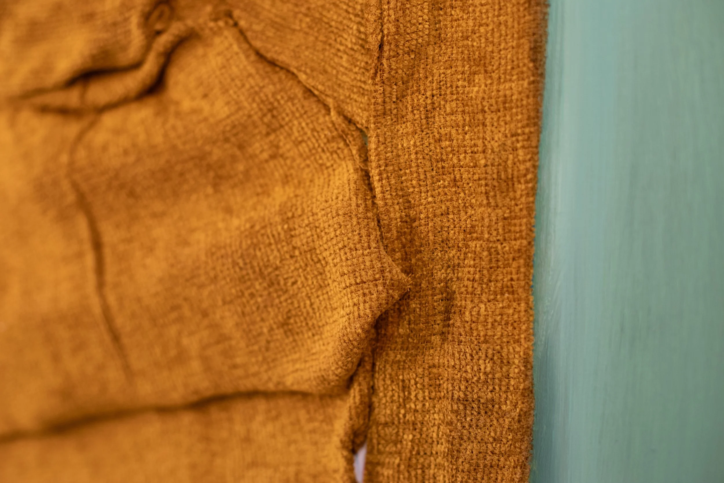 Ein weißer Stoff, der auf den Boden gelegt wurde, mit einigen Falten und Rissen. Im oberen linken Bereich ist ein Teil einer gebogenen, terrakottafarbenen Oberfläche sichtbar.