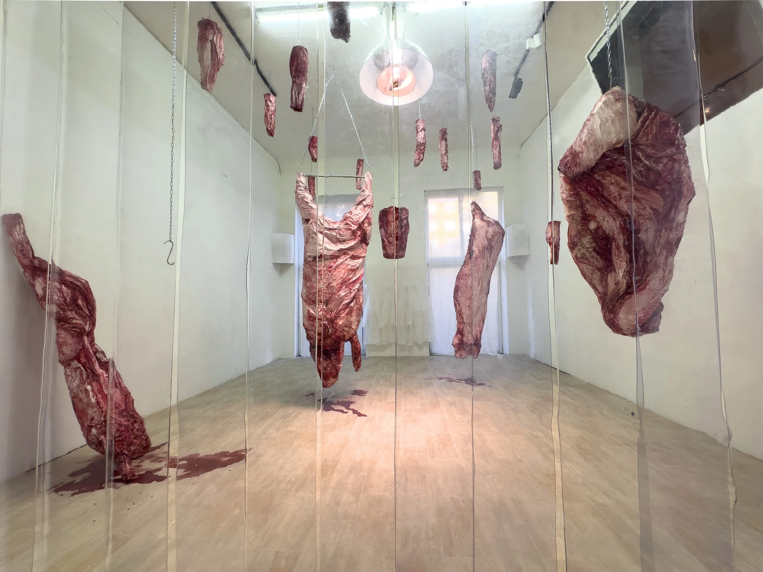 Installation mit große aufgehängte Fleischstücke in einer leeren Galerie mit Holzfußboden und weißen Wänden.