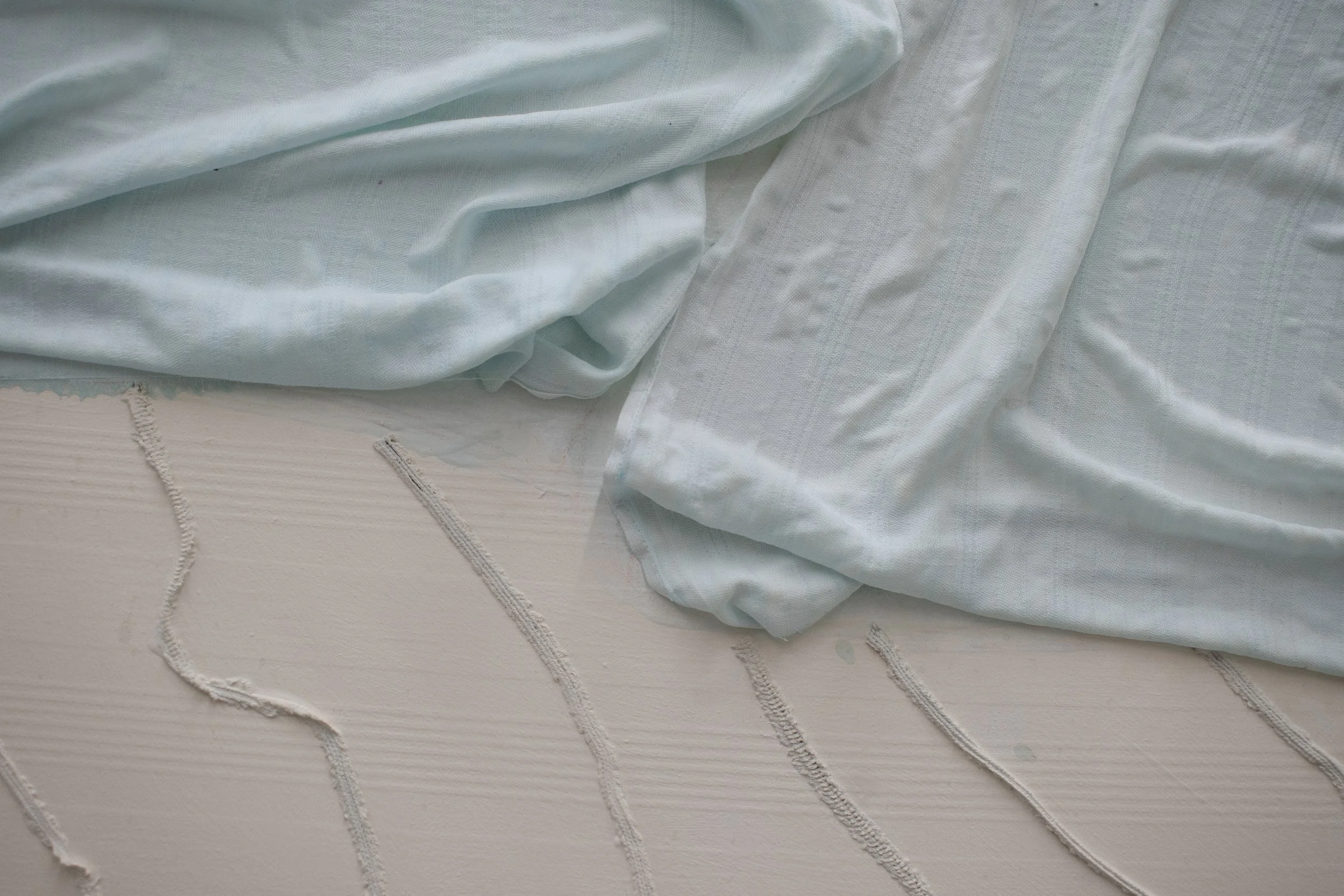 Verwüstete weiße Bettwäsche mit blauen Farbtupfern und Flecken, zerknittert und schmutzig.