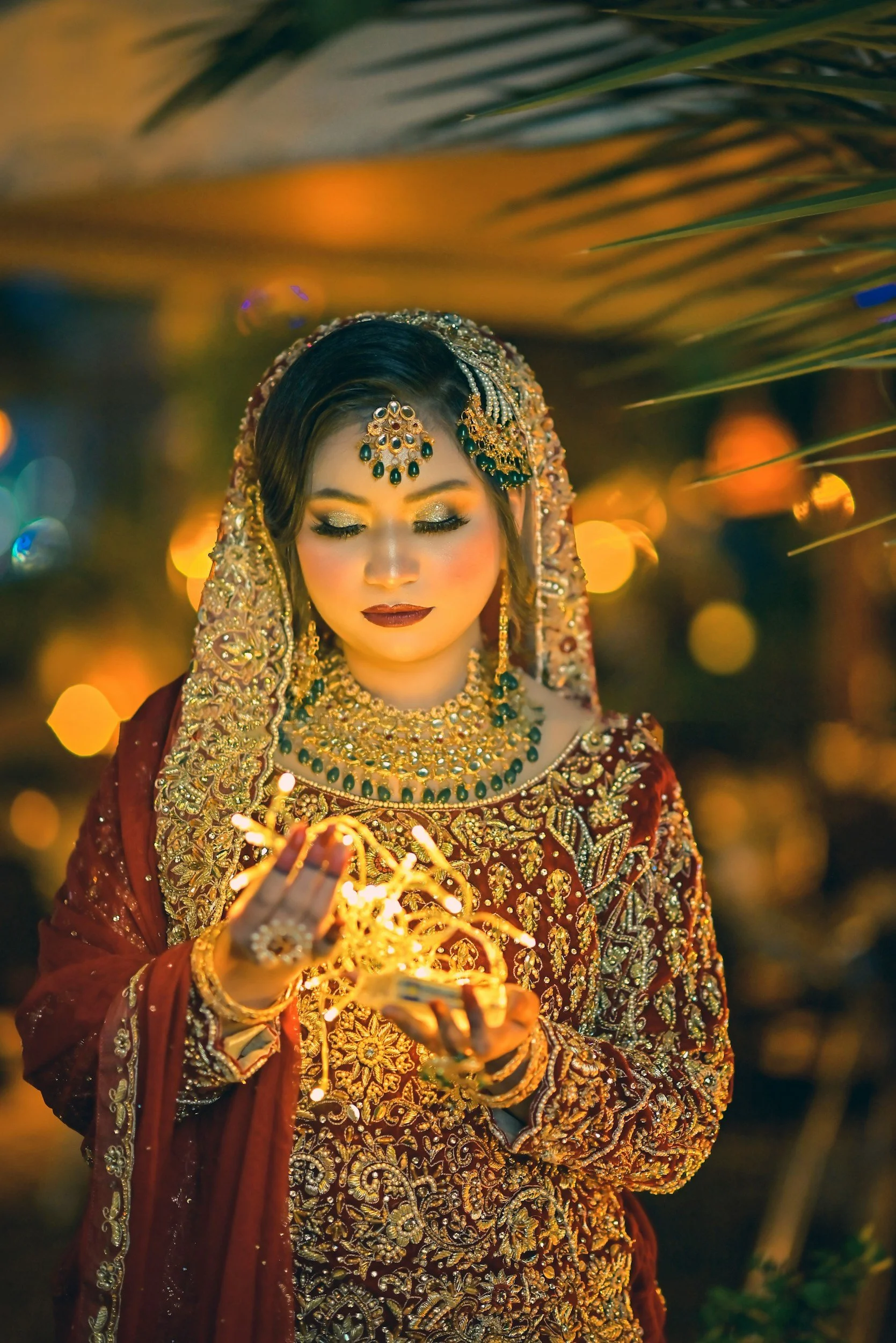 A woman dressed in traditional Indian bridal attire holding a lit string of lights, with a warm and glowing background.