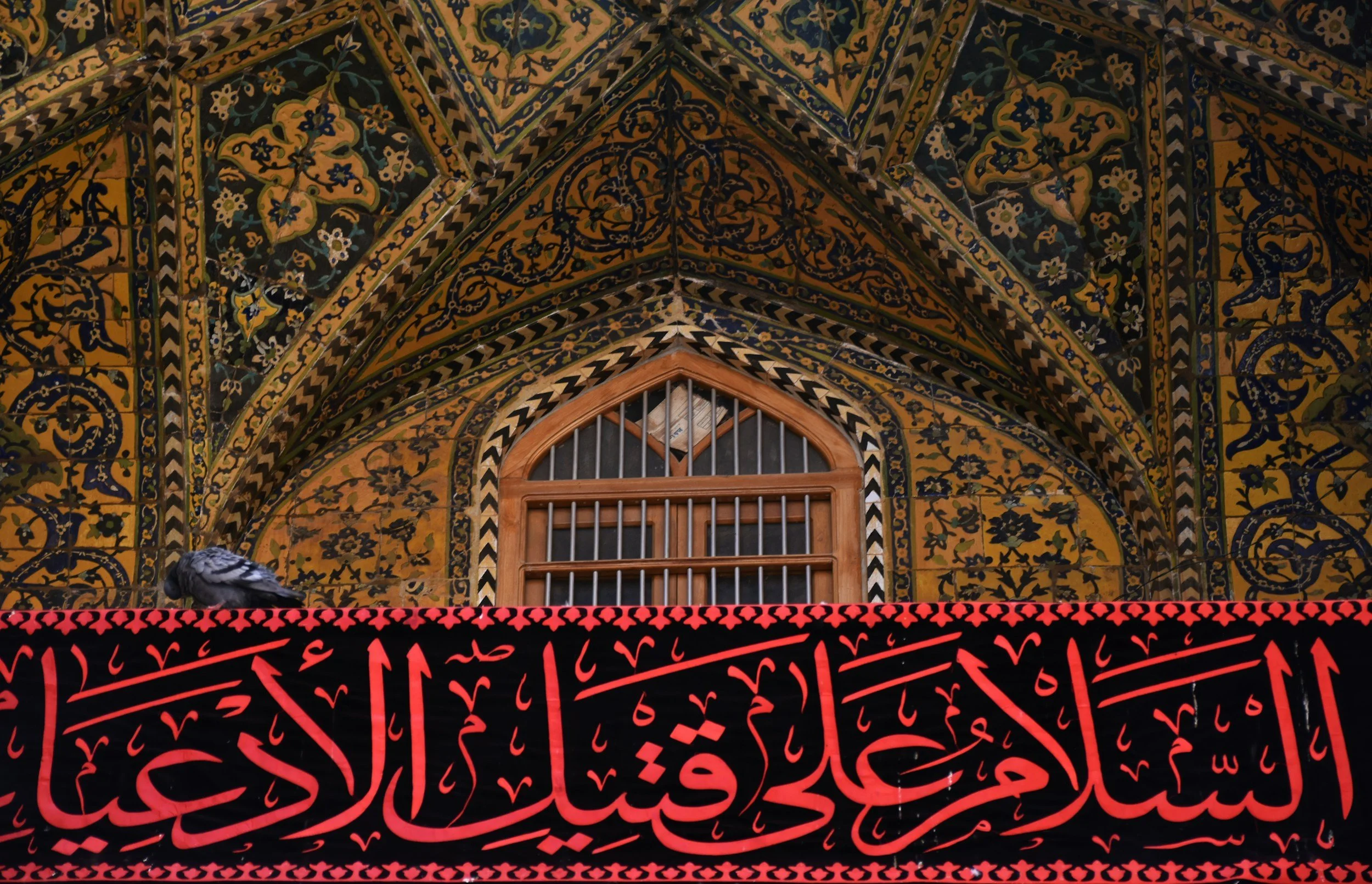 Decorative Islamic architecture with colorful tile patterns and Arabic calligraphy banner in red and black.