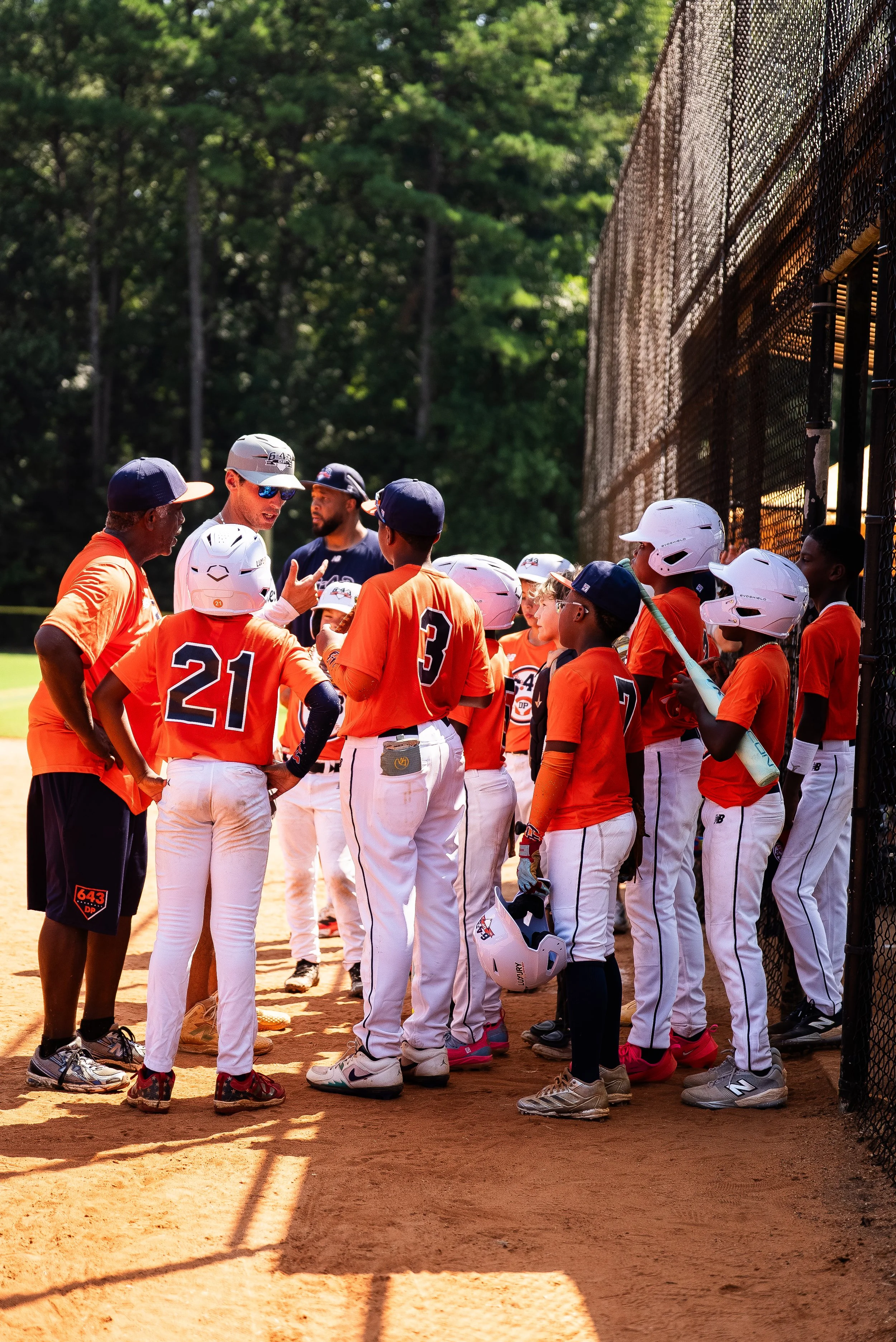 Little league baseball team gathered around coach during game or practice on baseball field.