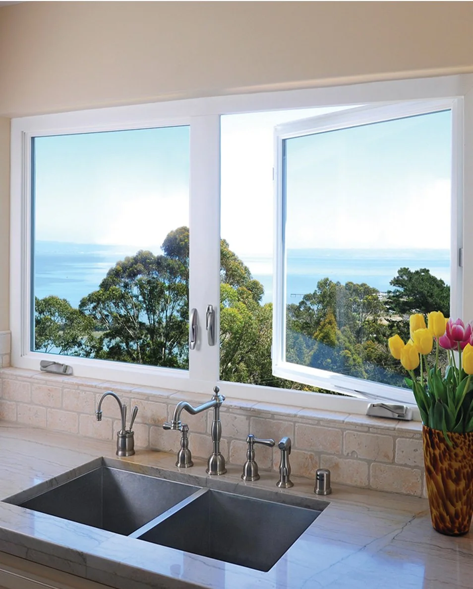 Kitchen sink with a view of trees and a body of water through an open window, with a vase of yellow and pink tulips on the right.