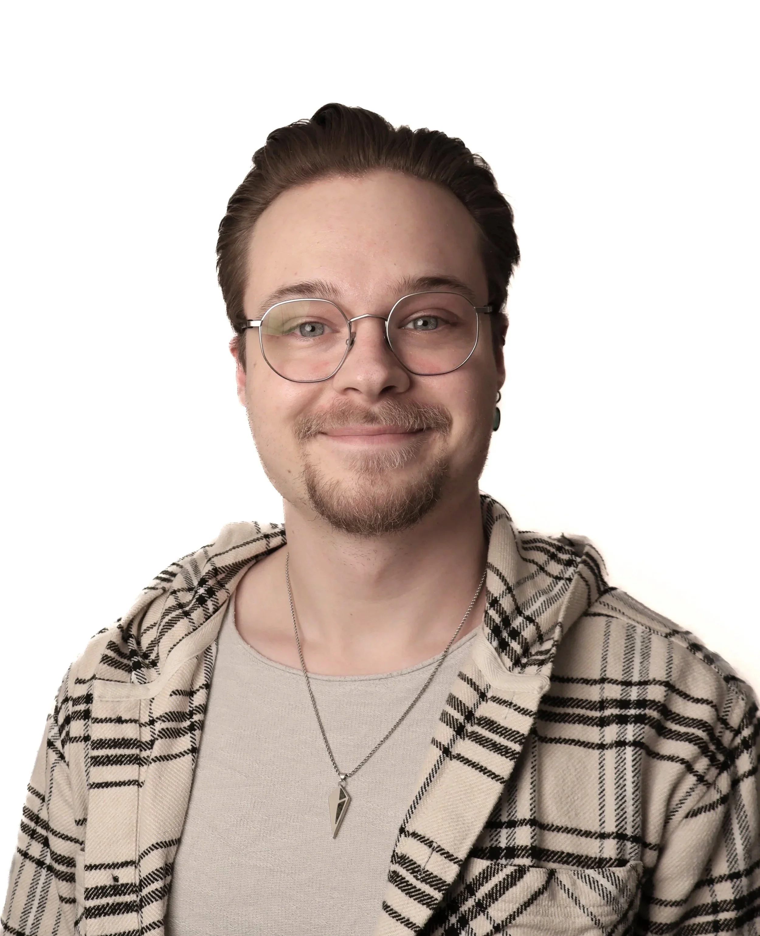 Ein junger Mann mit Brille, kurzen braunen Haaren, einem leichten Bart und einem Lächeln, trägt ein beige kariertes Hemd über einem hellen T-Shirt, mit einer Kette mit einem spitzen Anhänger.