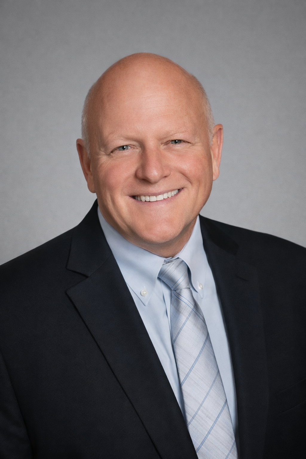 Smiling man in a suit and tie, posing for a professional headshot against a neutral background.