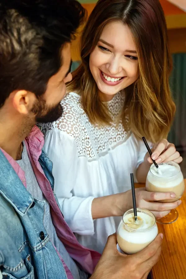 A woman and a man smiling and talking while holding drinks in a cozy, well-lit cafe or bar.