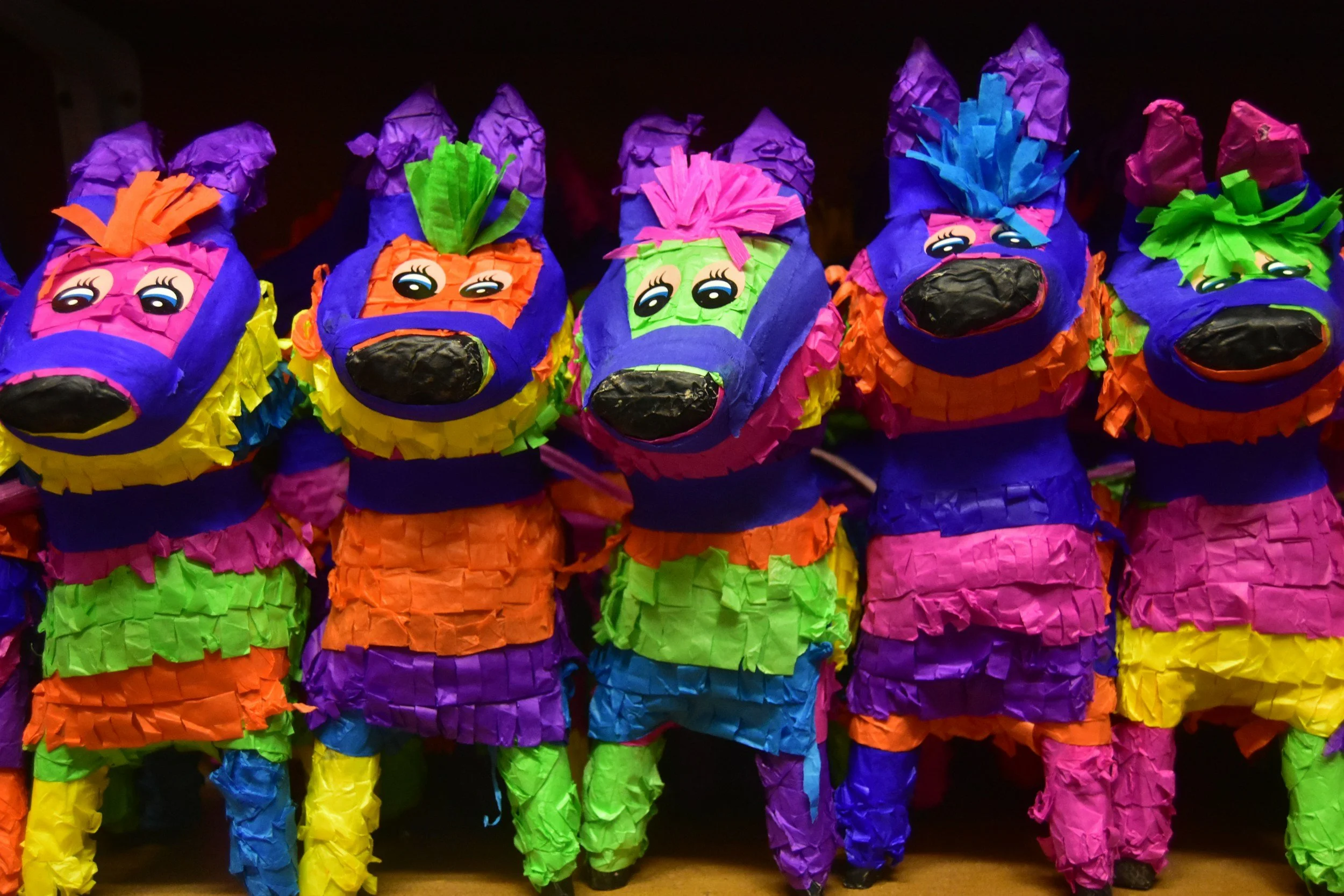 Colorful piñatas shaped like chickens with cartoonish faces, decorated with vibrant tissue paper in colors purple, pink, orange, green, blue, and yellow.