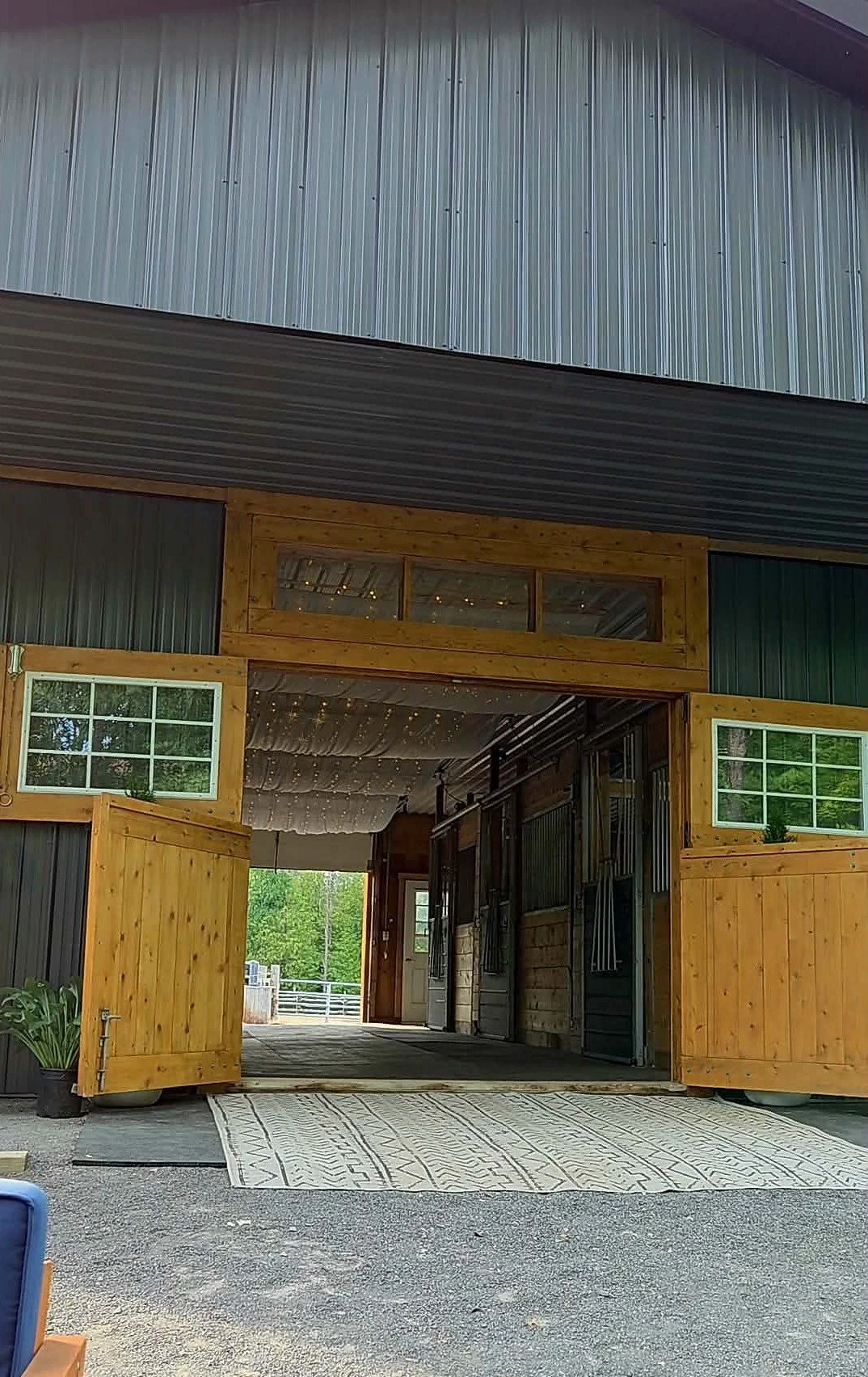 A large barn with a partially open front, featuring wood and metal siding, windows, and a gravel driveway.