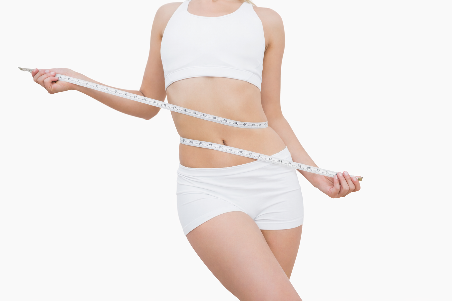A woman in white sportswear measuring her waist with a tape measure against a plain white background.