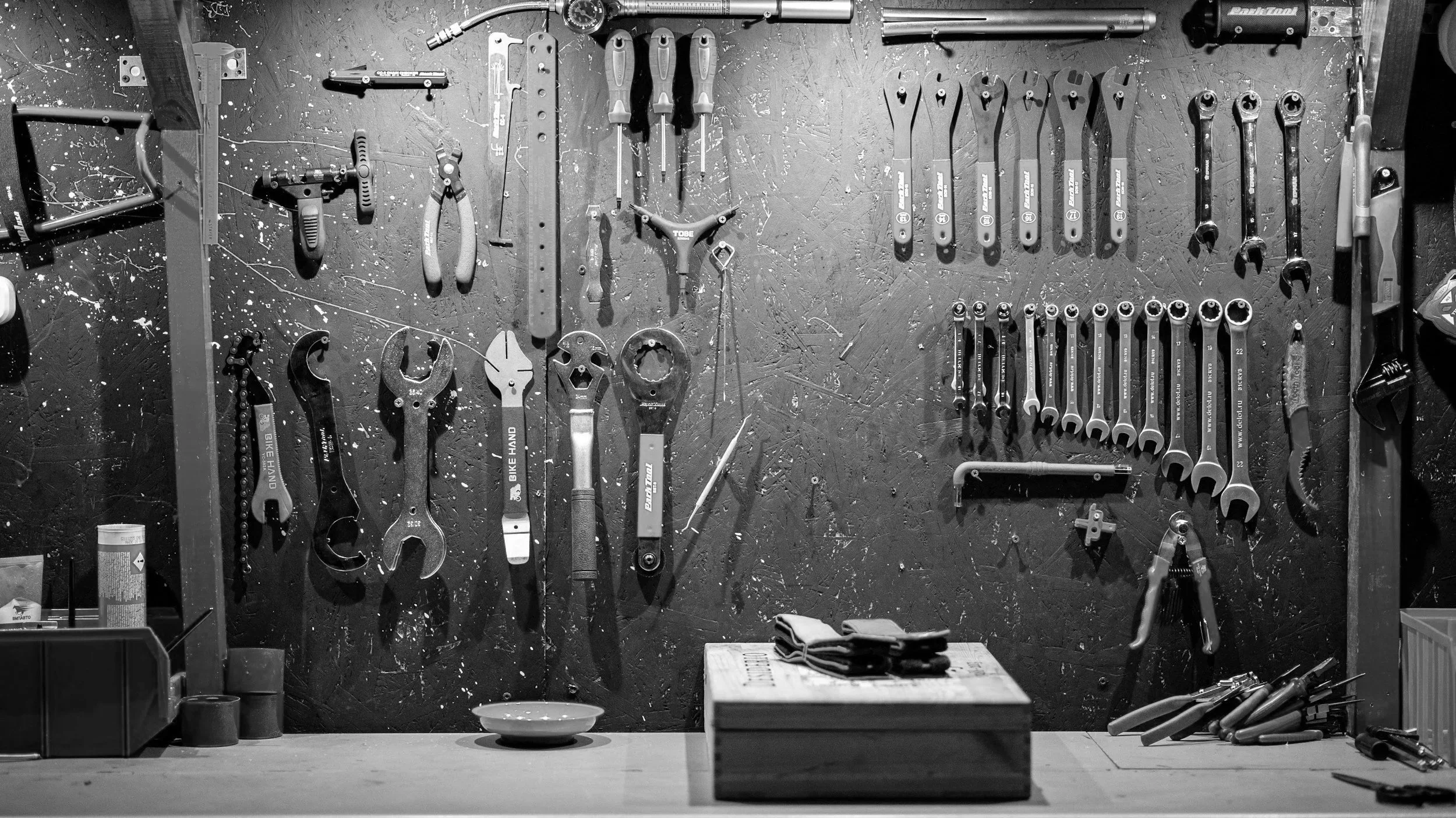 Black and white image of a wall-mounted organized toolbox with various hand tools, including wrenches, screwdrivers, and pliers, on a workbench.