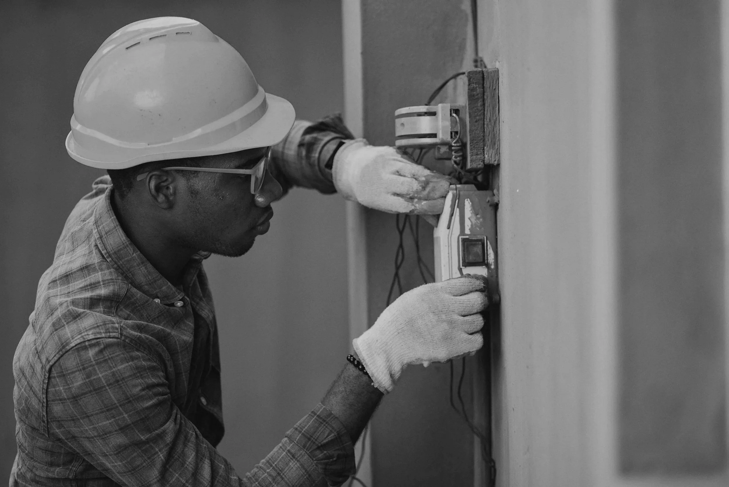 A man wearing a hard hat and safety gloves working on electrical wiring on a wall.