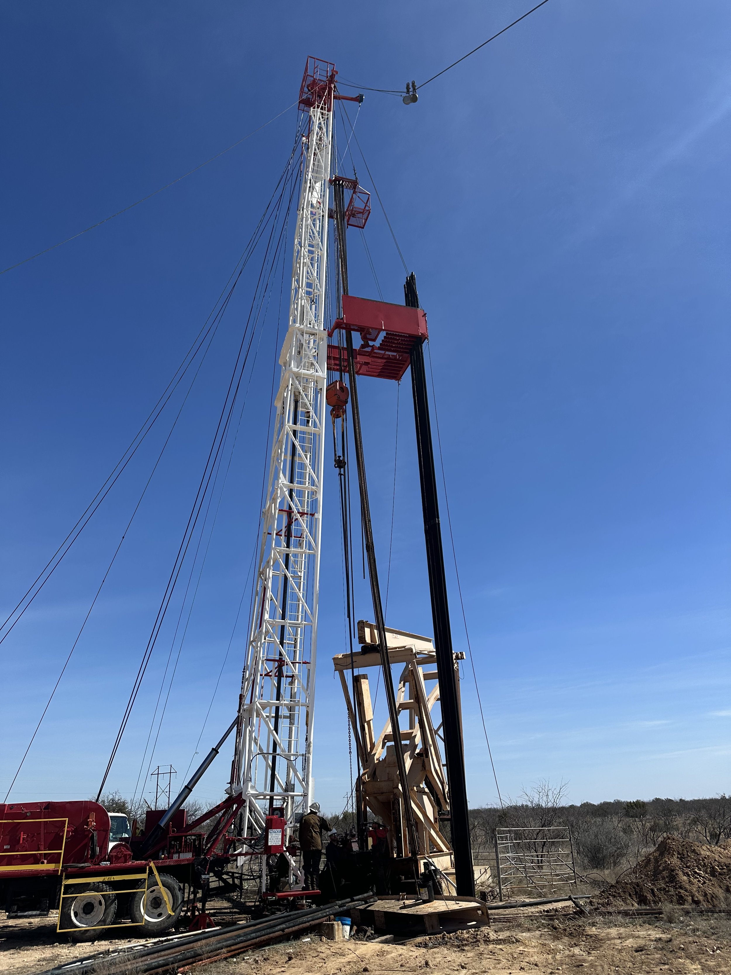 An oil drilling rig with a tall white and red tower under a clear blue sky.