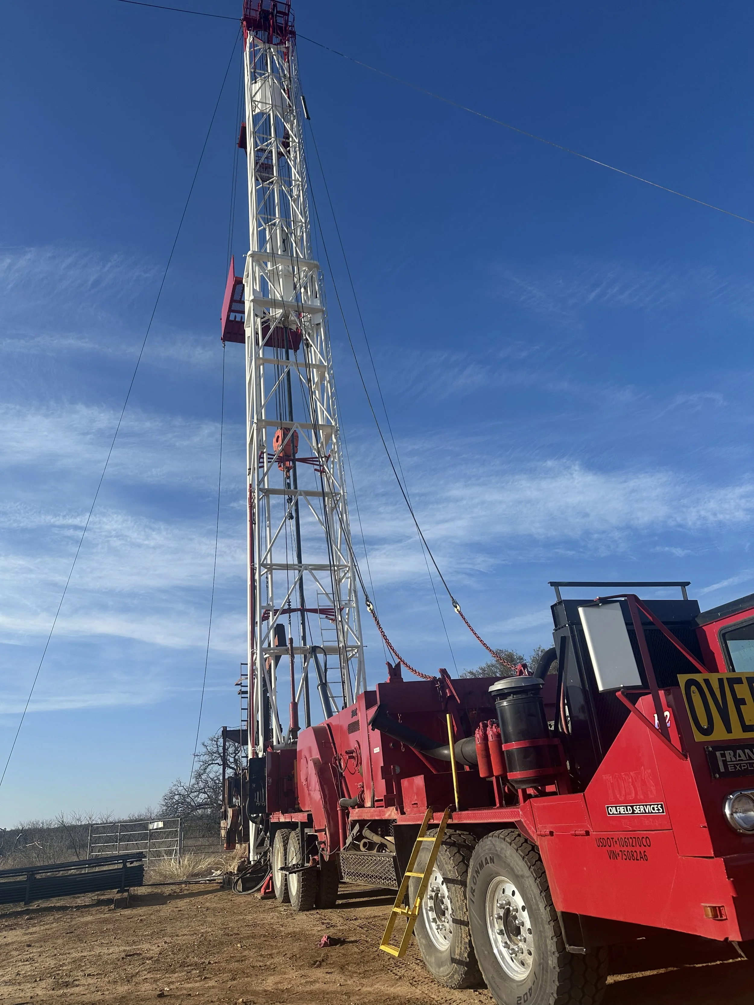 A large red and white oil drilling rig truck on a dirt lot with a clear blue sky in the background.