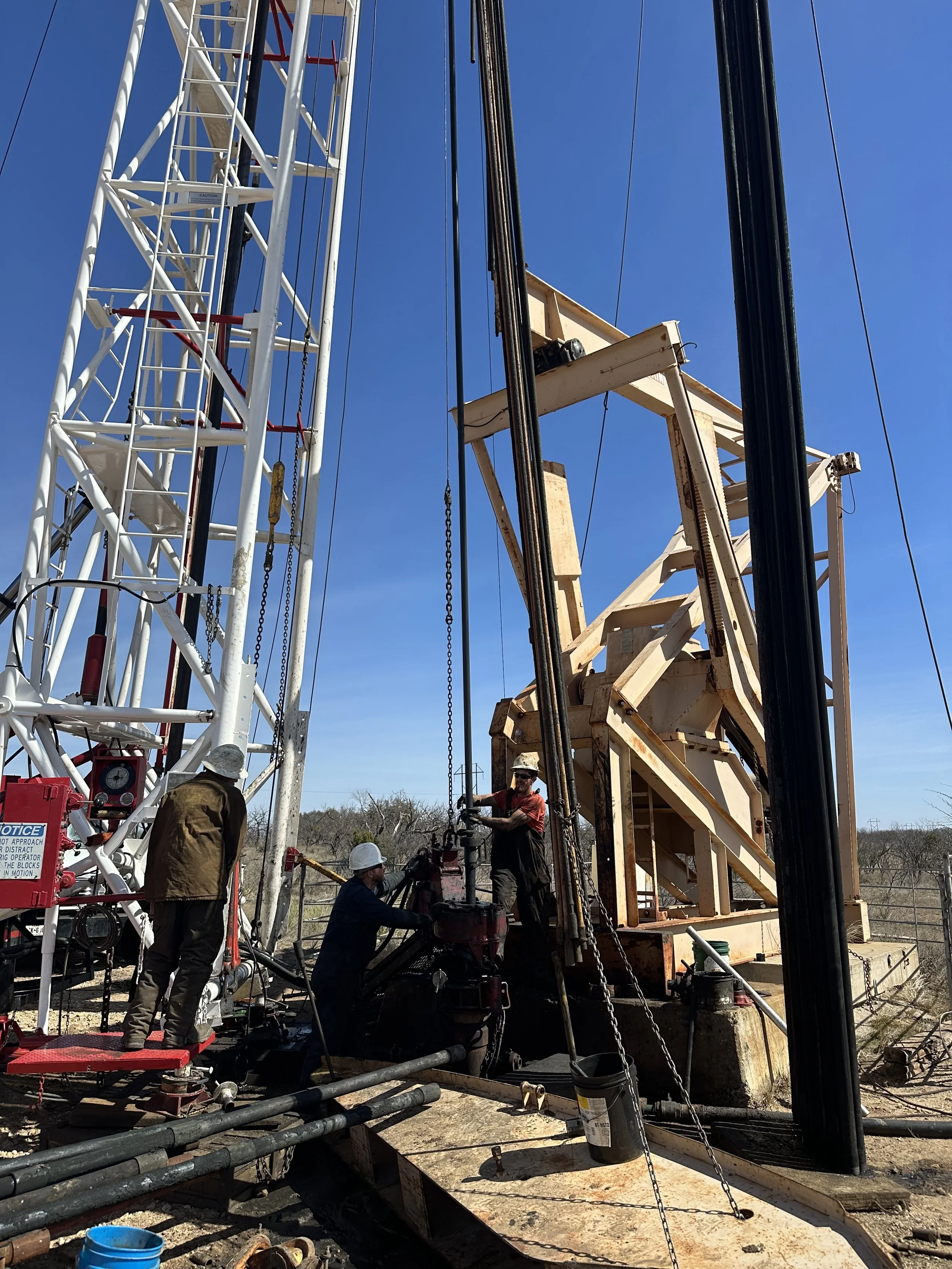 Workers operating drilling equipment on an oil rig against a clear blue sky.