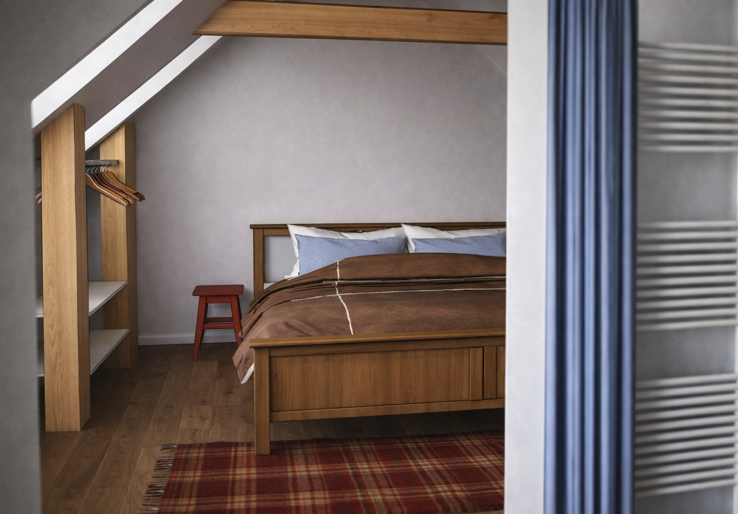 View of a cozy bedroom with a wooden bed, blue pillows, a brown duvet, small red side table, and a wooden shelving unit, with a plaid rug on wooden floor and a sloped ceiling.