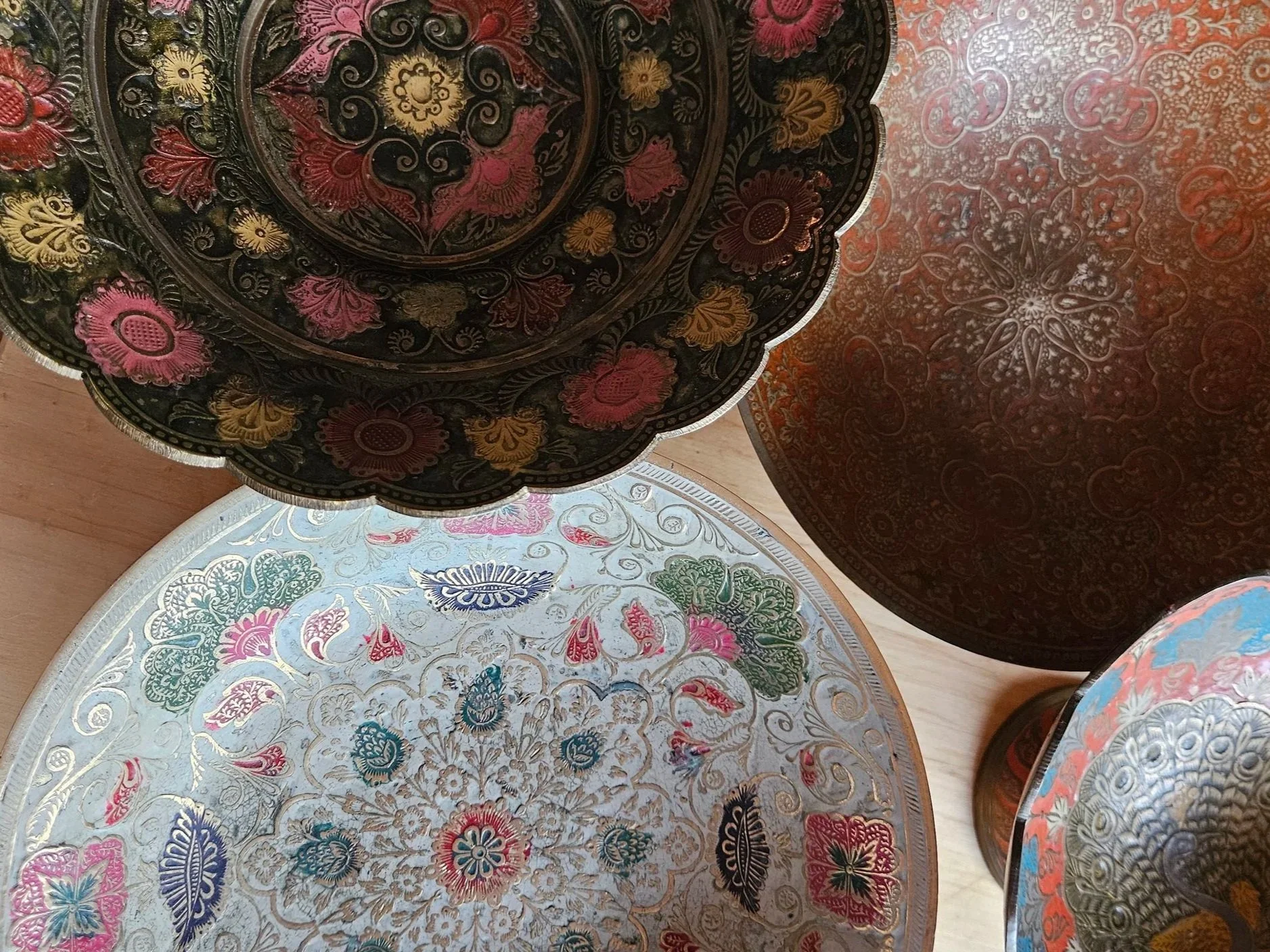 Decorative metal trays with intricate floral patterns and vibrant colors, stacked together.