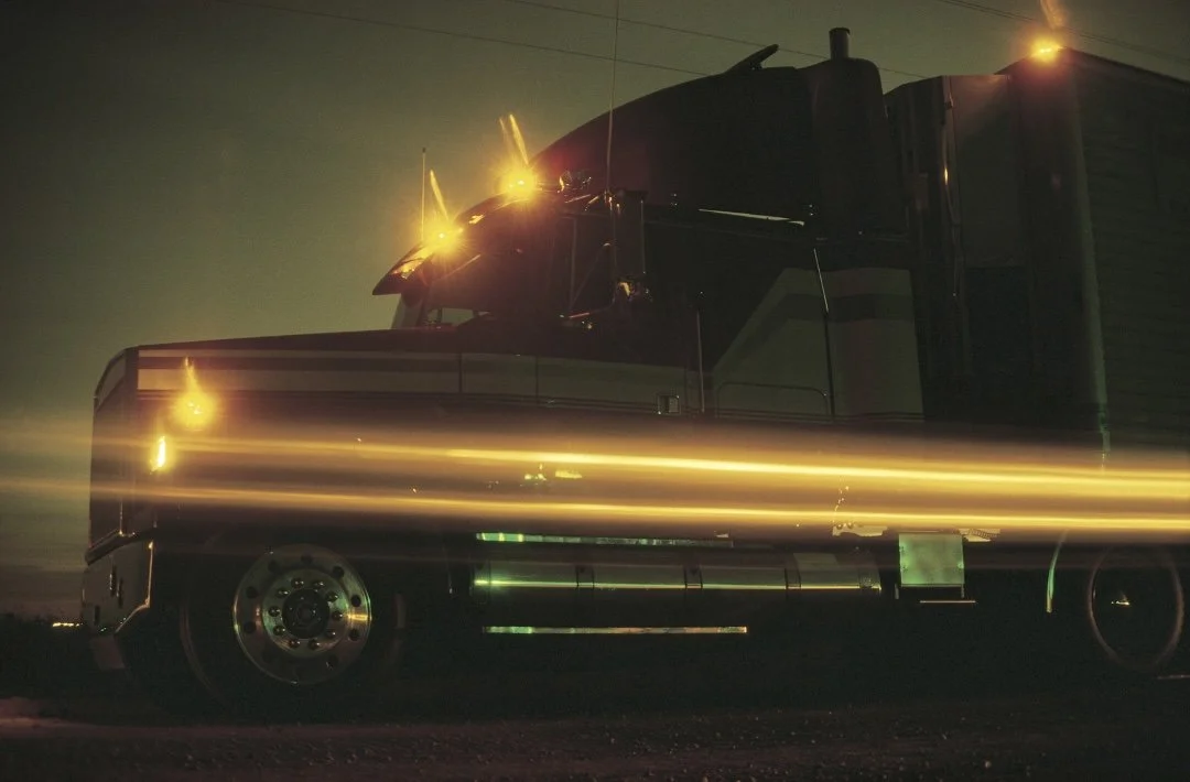 A large semi-truck at night with glowing yellow lights and streaks of light in front of it.