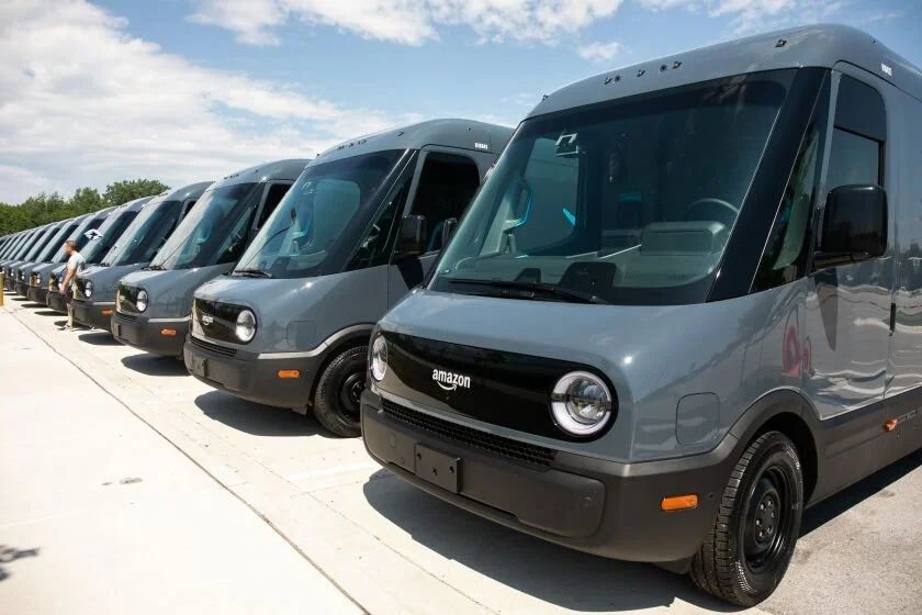 Multiple Amazon delivery vans parked in a lot under a partly cloudy sky.