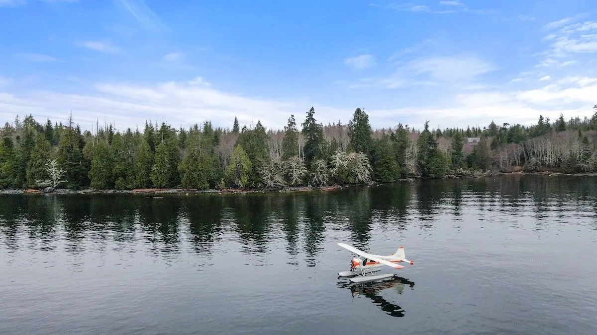 Orange and white seaplane peacefully floating on a calm ocean day, capturing the tranquil essence of Vancouver Island waterfront living and the beauty of waterfront properties for sale.