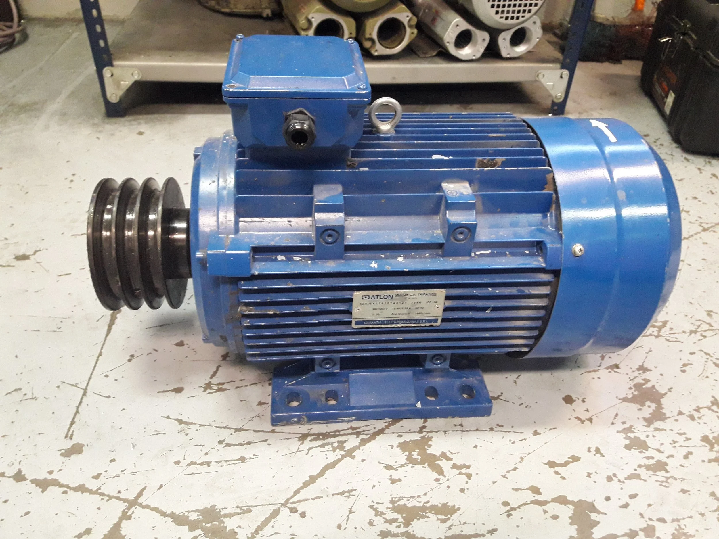 Motor eléctrico azul con carcasa metálica y polea en un taller