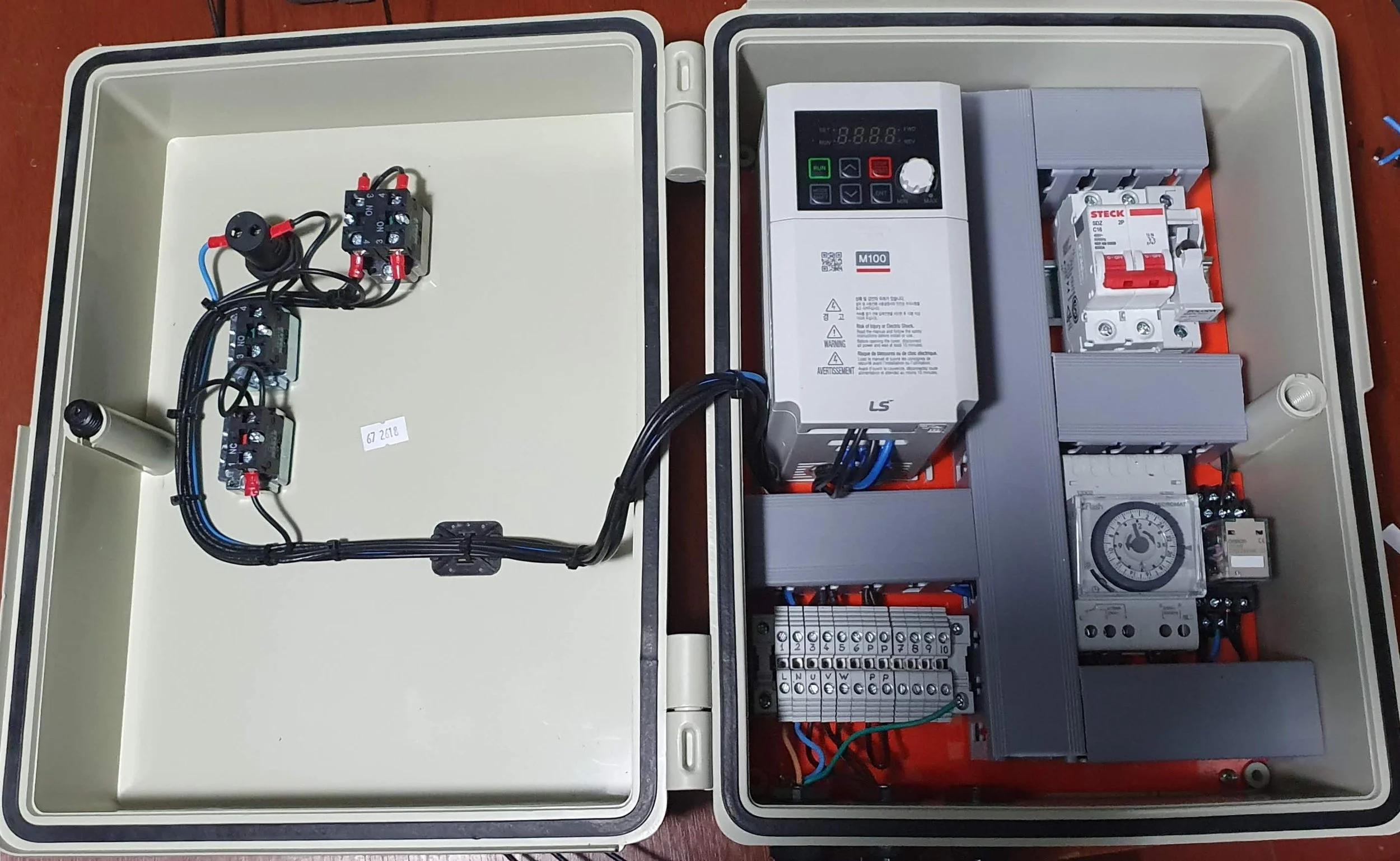Caja de control eléctrica con componentes electrónicos y dispositivos de automatización, incluyendo variador de frecuencia, relés y temporizador, visible en su interior.