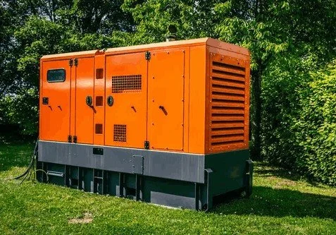 Generador eléctrico de color naranja en un área al aire libre con árboles verdes en el fondo.