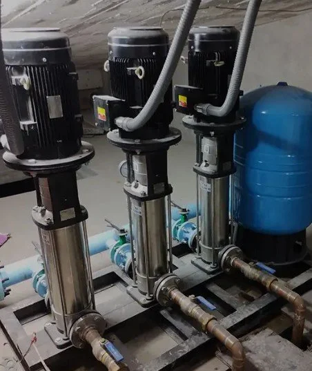 Tres bombas de circulación de agua con motor eléctrico, tubos de conexión y una ligera línea gris en un ambiente industrial.