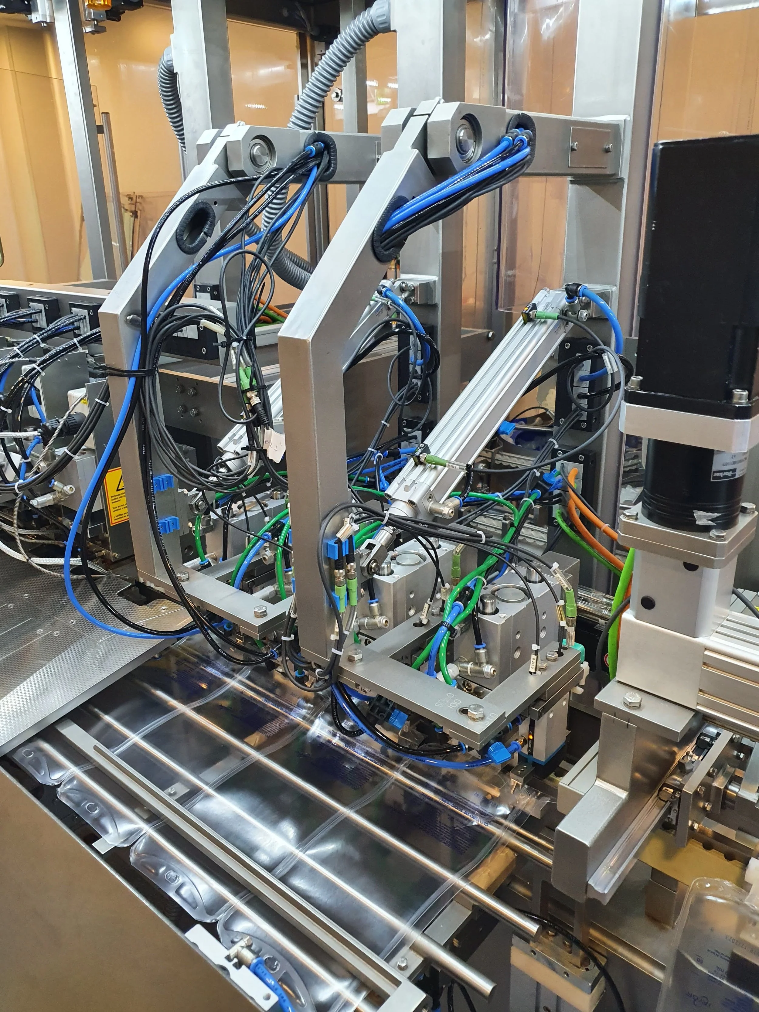 Imagen de una máquina industrial con componentes metálicos, cables y tubos en un entorno de fábrica.