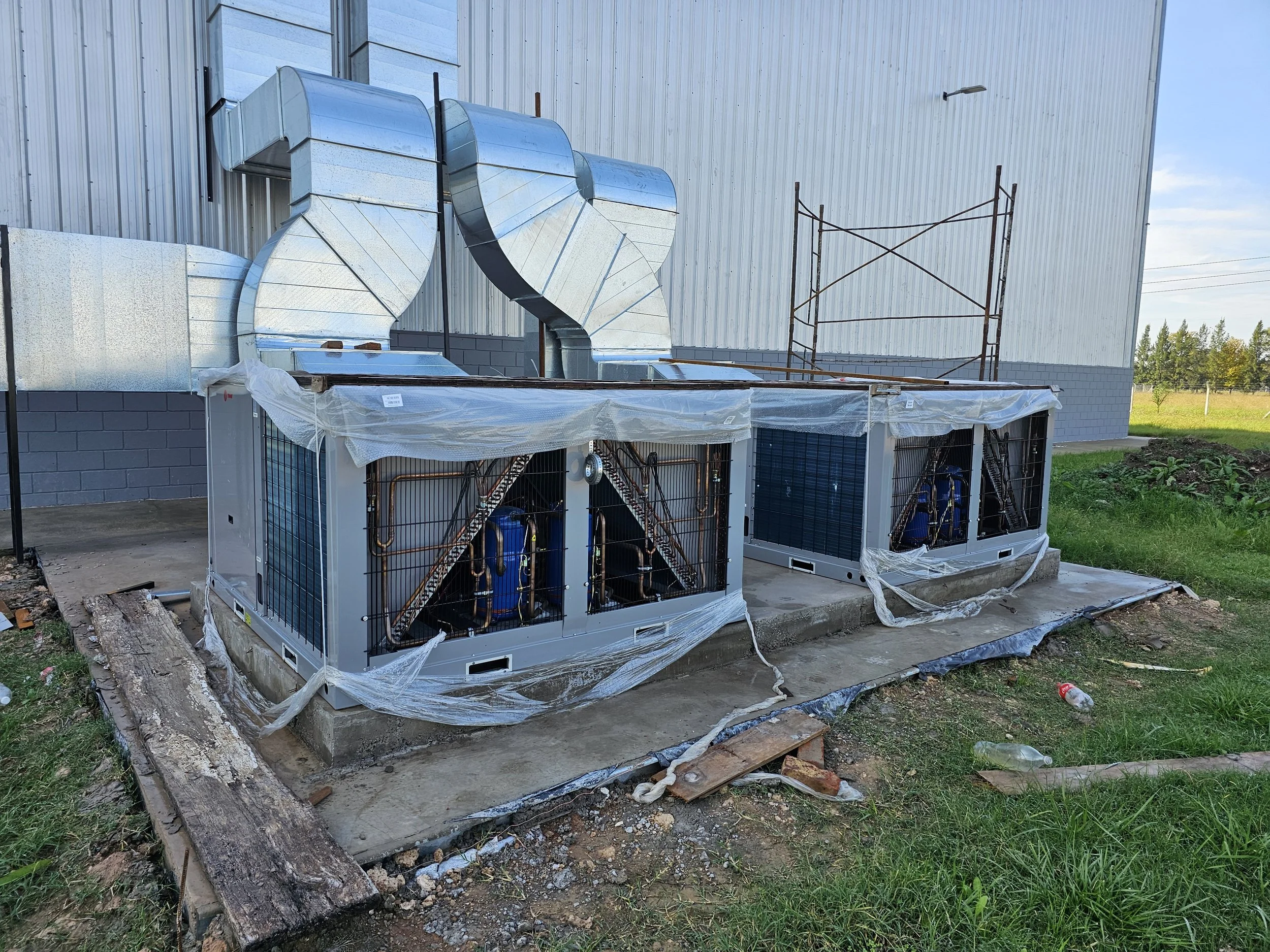 Un sistema de aire acondicionado industrial en instalación exterior junto a una estructura de metal y aire acondicionado en proceso de instalación