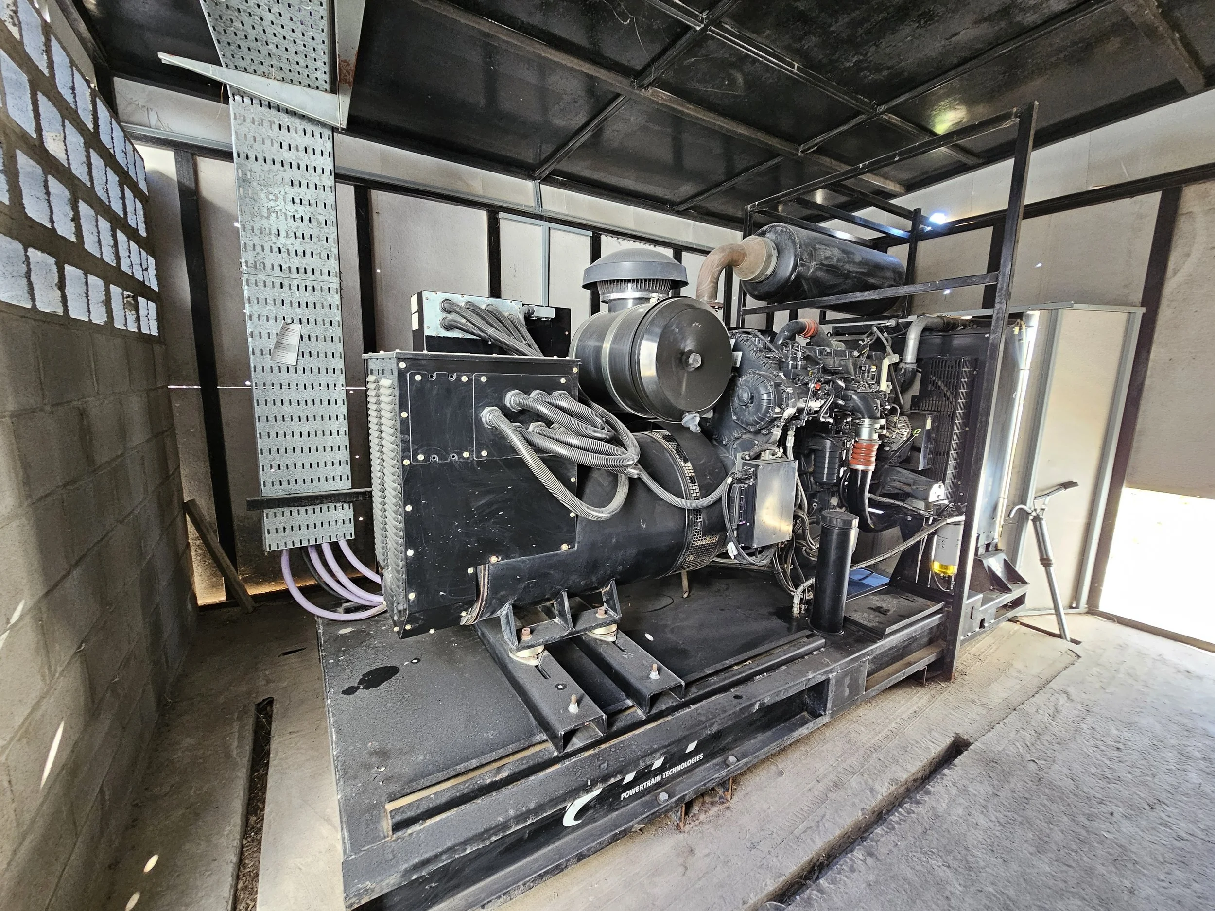 Generador industrial negro con componentes metálicos en un espacio cerrado.