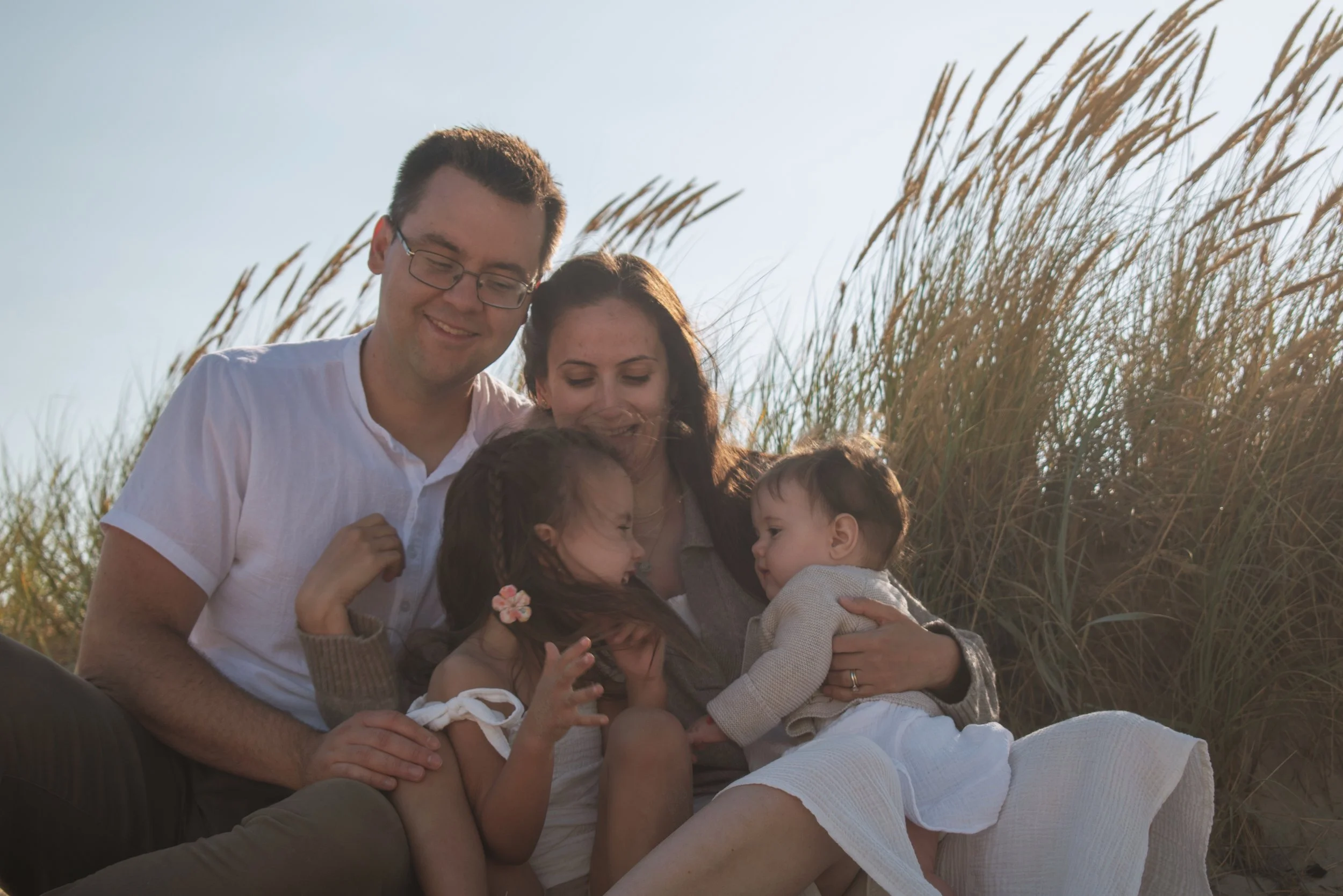 A happy family of four sitting outdoors near tall grass, enjoying a sunny day.