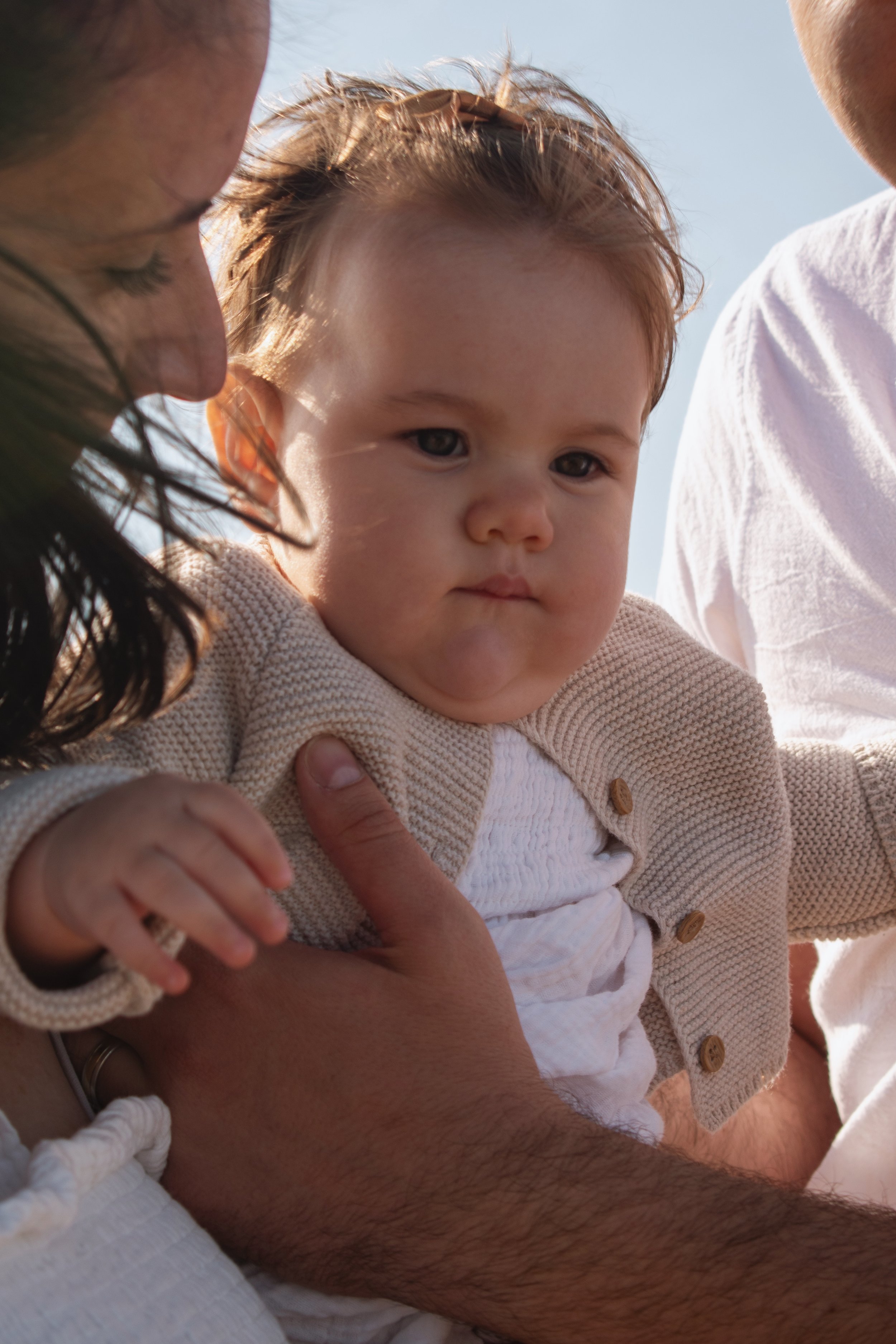 Close-up of a young child being held by parents, with a clear blue sky in the background.