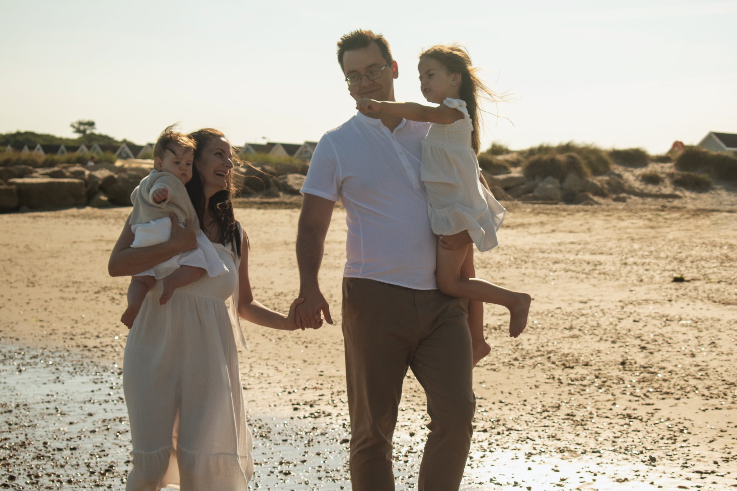 Family walking on the beach holding hands with two children, the sun setting in the background.