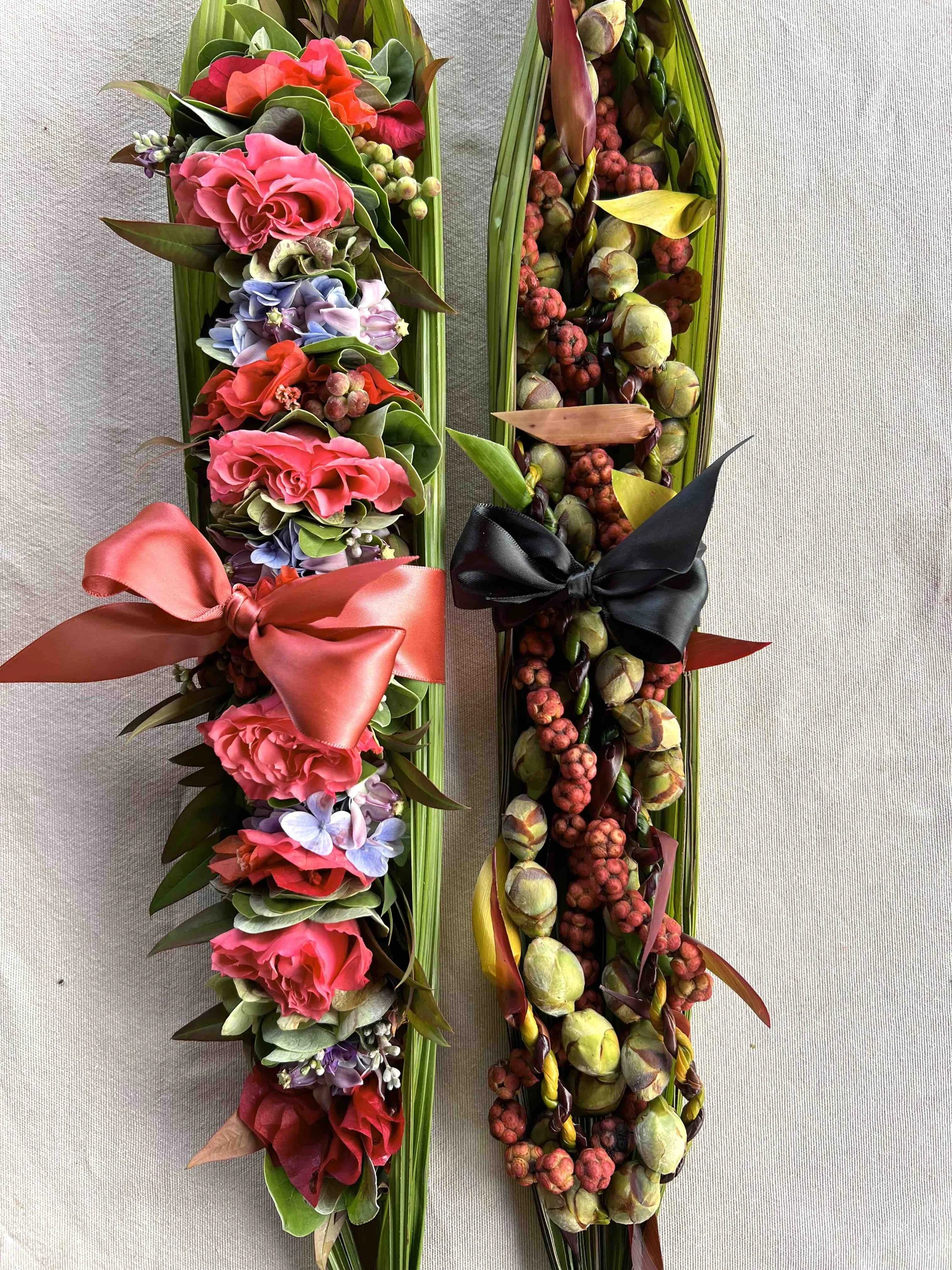 Colorful floral and fruit arrangements with pink, purple, and red flowers on the left and green, red, and purple fruits on the right, both decorated with large satin bows.