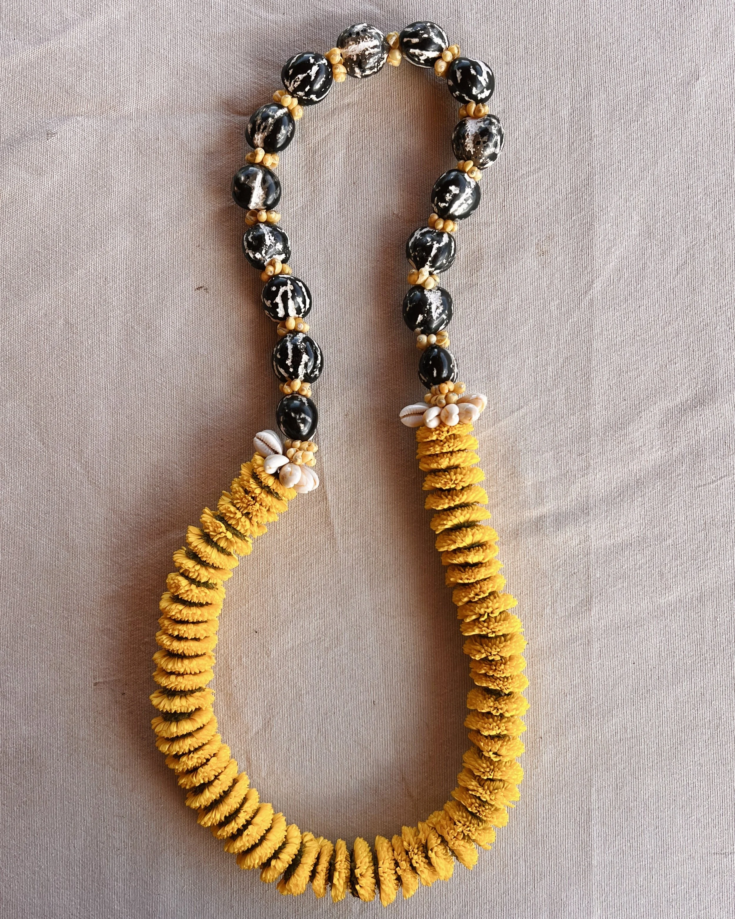 A decorative necklace made of black and white beads with yellow flowery accents, laid out on a beige surface.