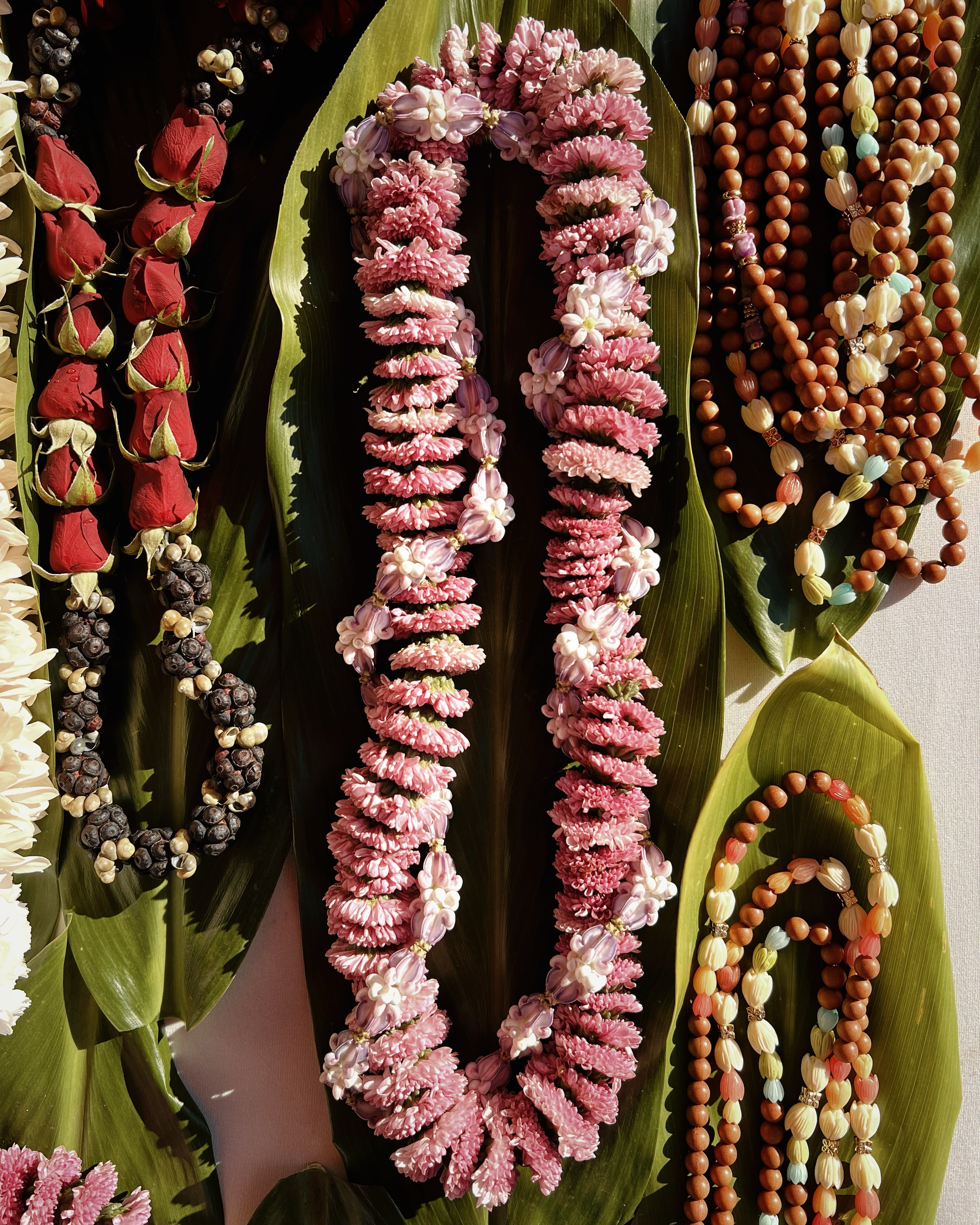 Colorful Hawaiian flower leis and necklaces on large green leaves.